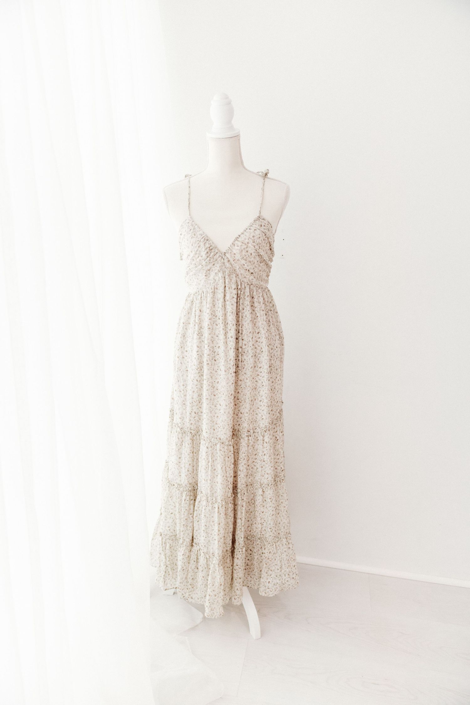 Cream floral spaghetti strap maxi dress with tiered ruffle skirt on white mannequin.