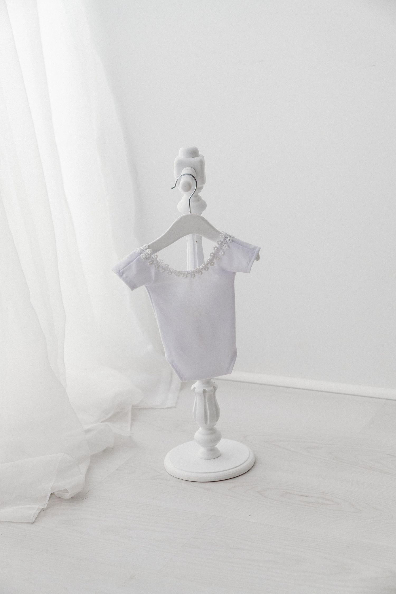 White short-sleeve baby bodysuit with ruffle collar detail on a white decorative mini clothing stand.