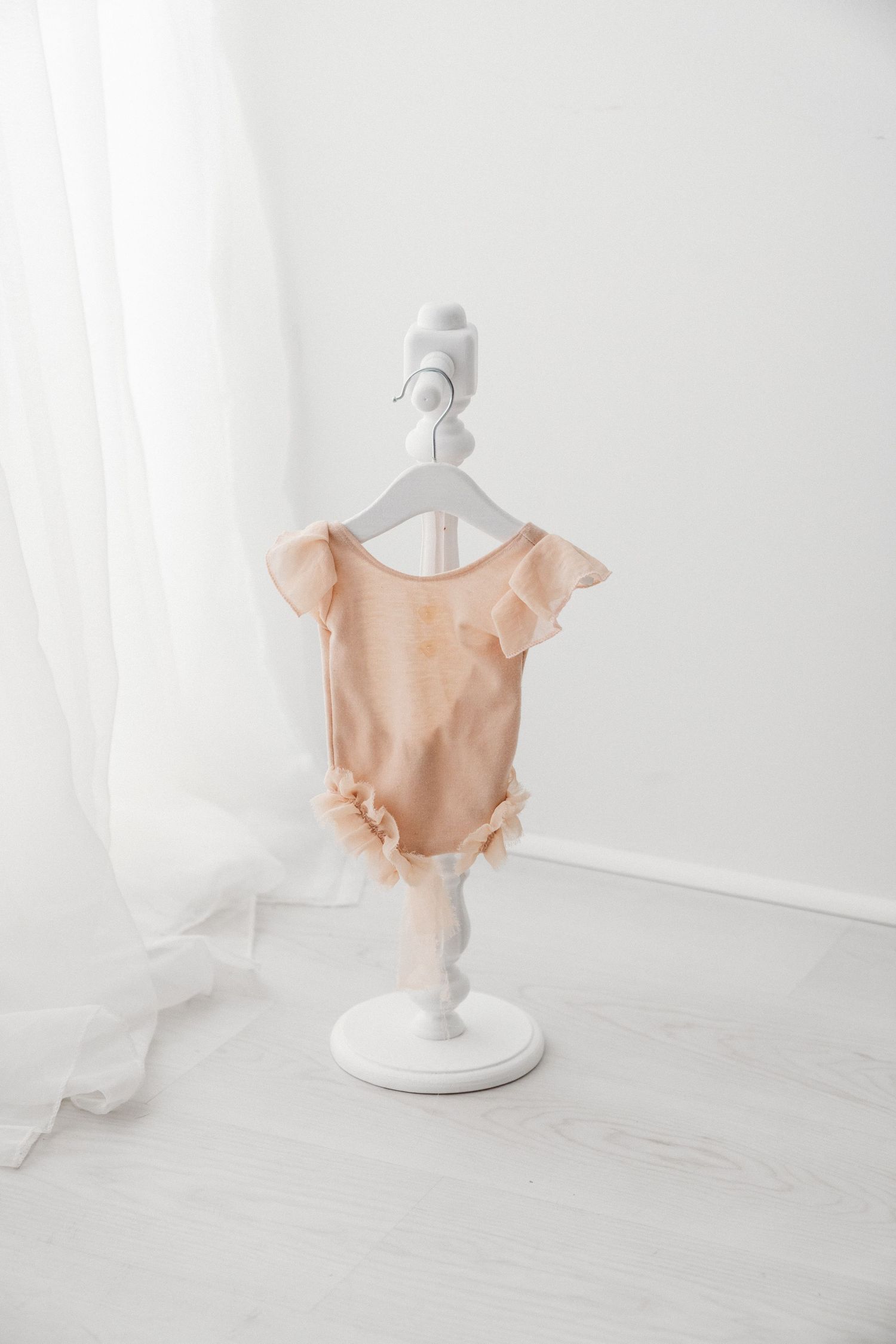 Peach satin baby bodysuit with flutter sleeves and ruffle hem on a white decorative stand.