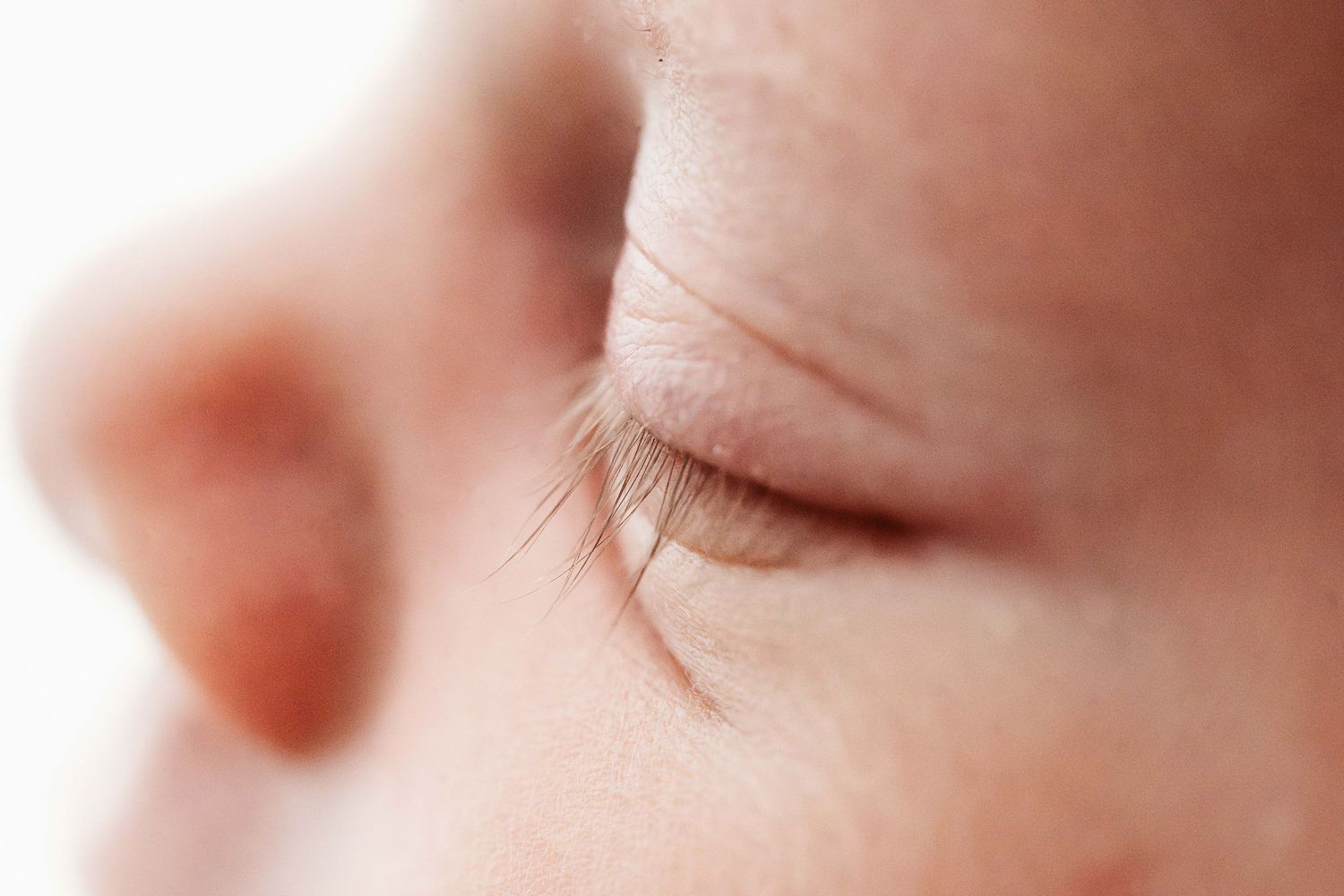 An extreme close-up macro photo of a newborn baby's closed eye with delicate eyelashes visible.