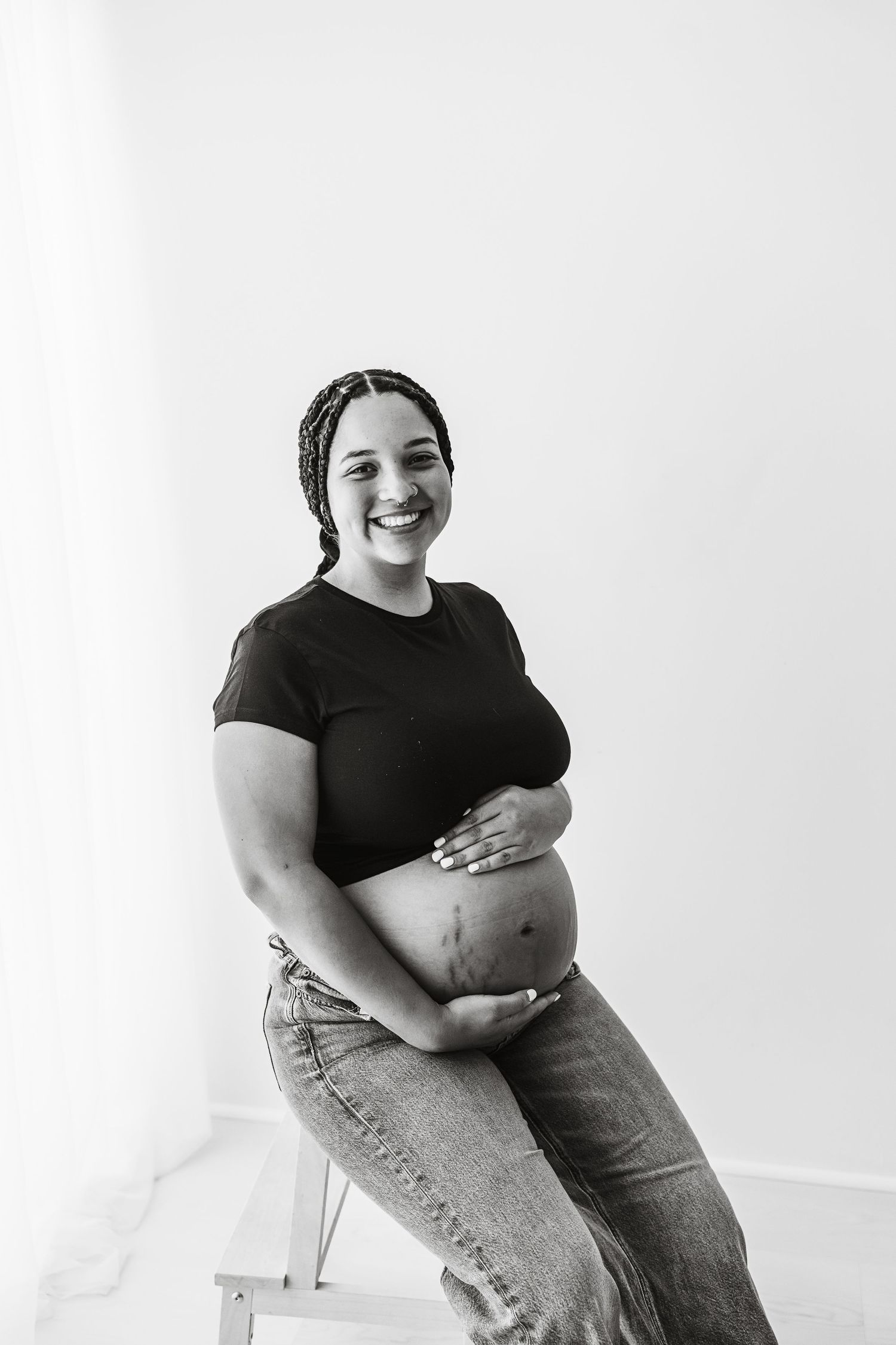 Black and white portrait of a smiling pregnant woman in black top and jeans holding her belly.