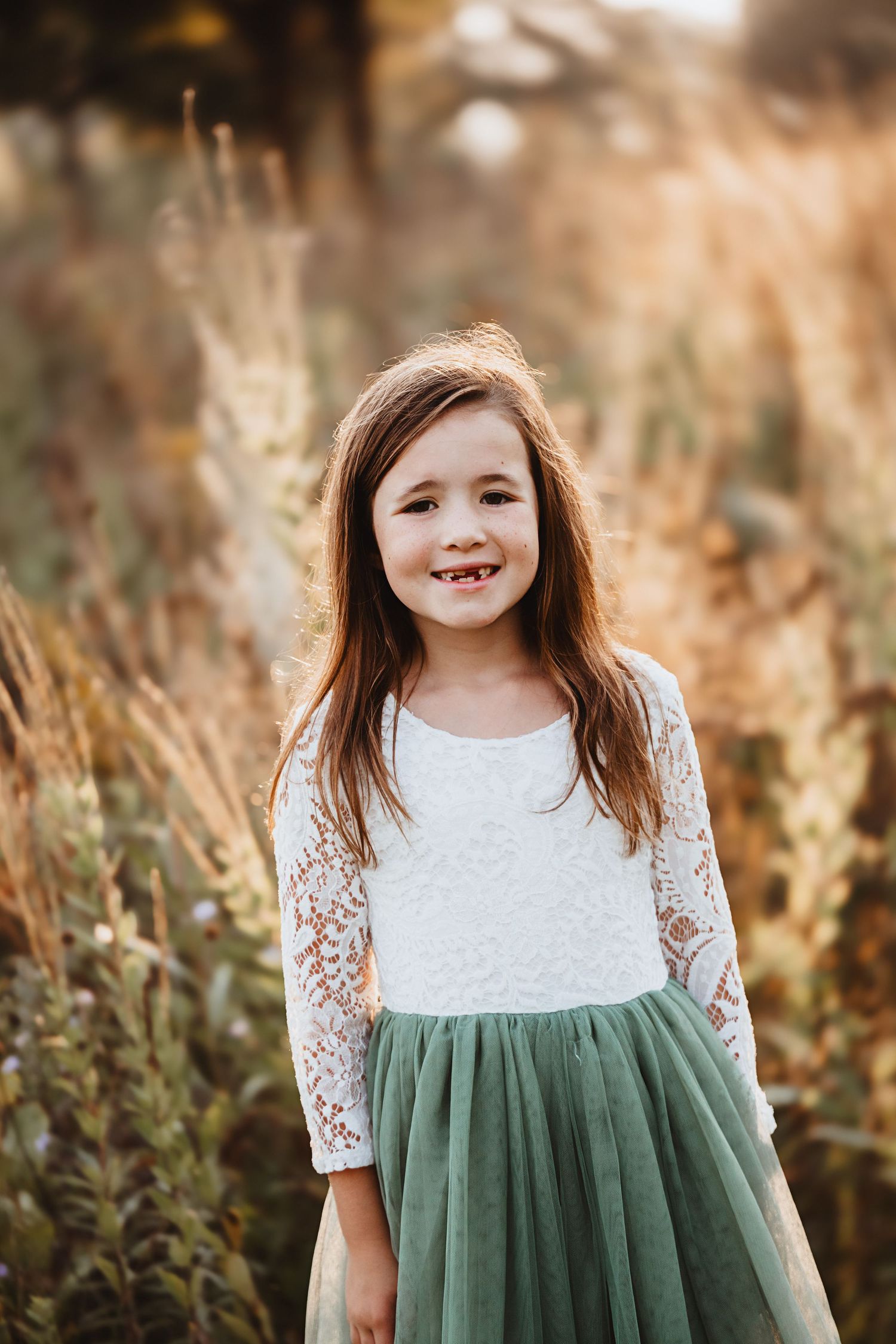 Smiling young girl in white lace dress and green tulle skirt in golden field.