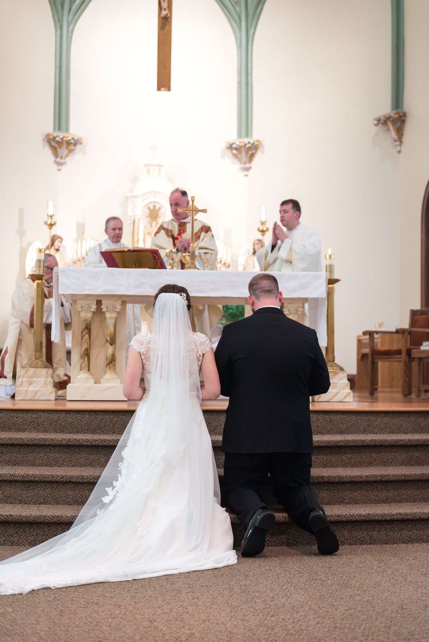 Bride and groom kneel at church altar during traditional Catholic wedding ceremony.