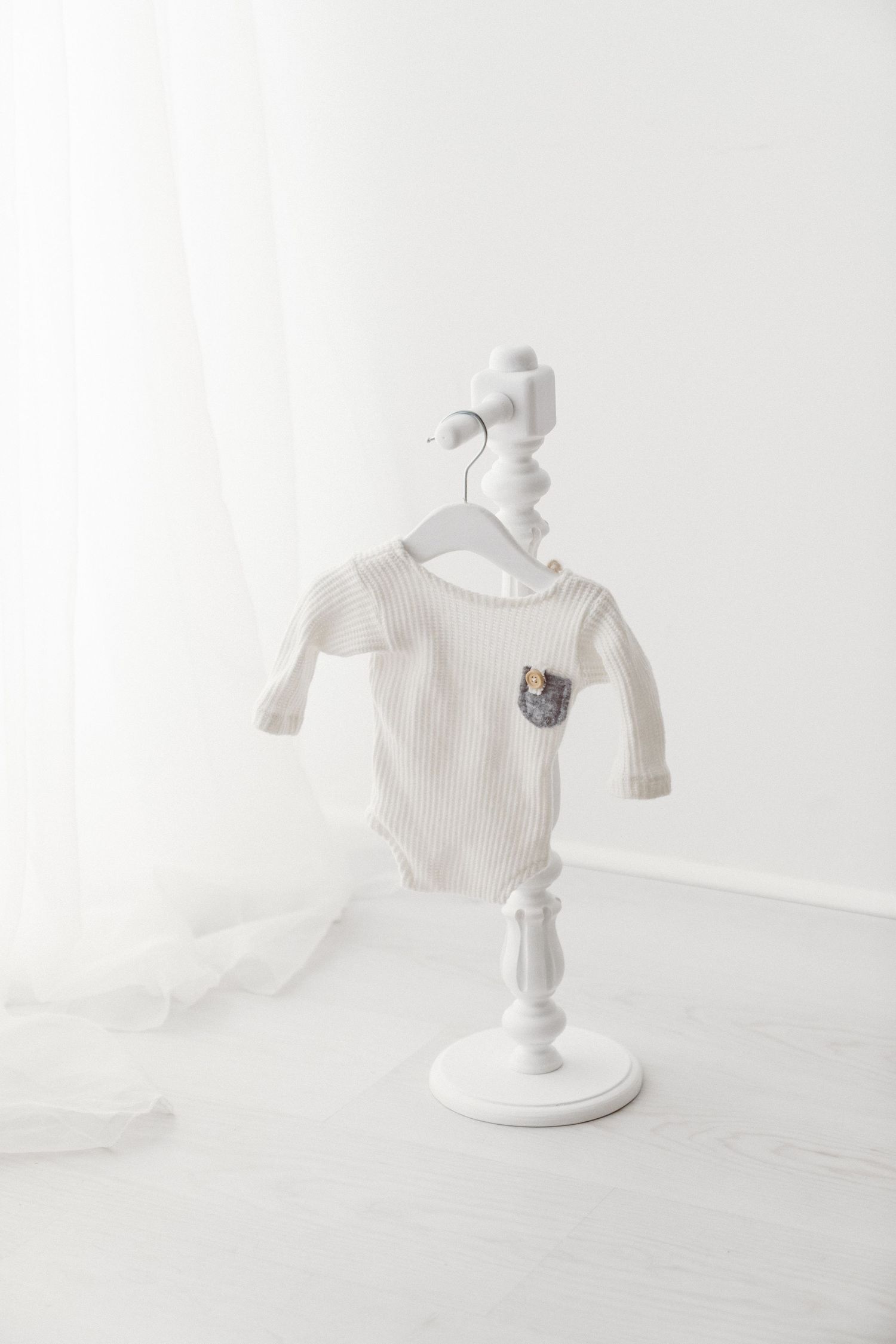 Cream ribbed long-sleeve baby bodysuit with patterned pocket on a white decorative stand.