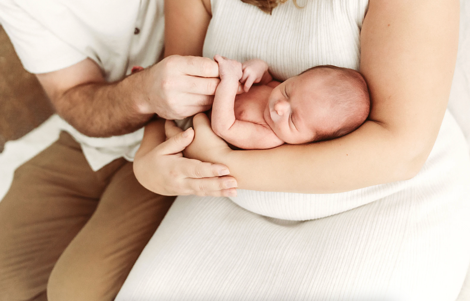 Couple gently holding curled sleeping newborn baby in their arms in soft studio portrait.