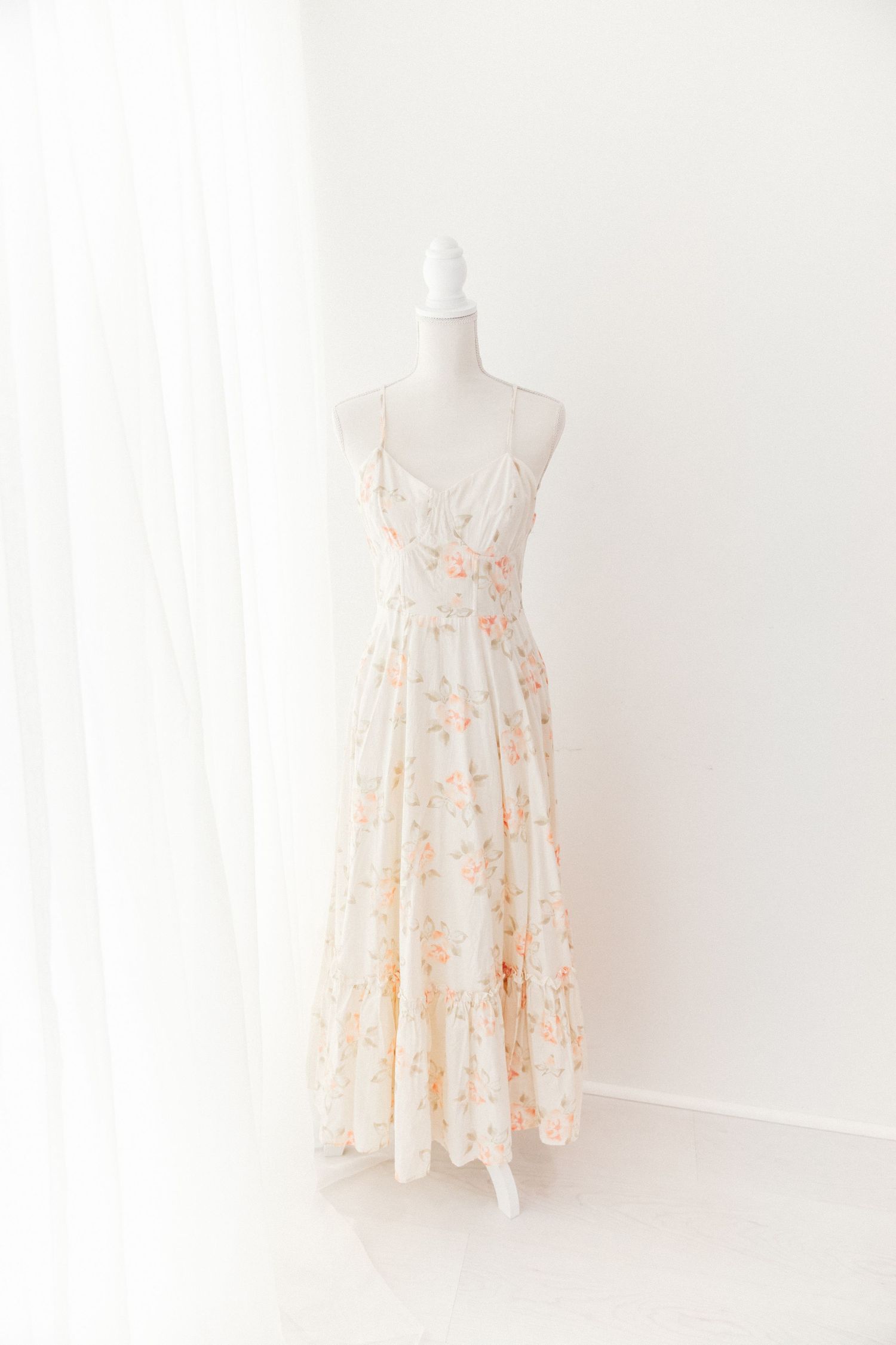 Cream orange floral spaghetti strap maxi dress with ruched bodice on mannequin.