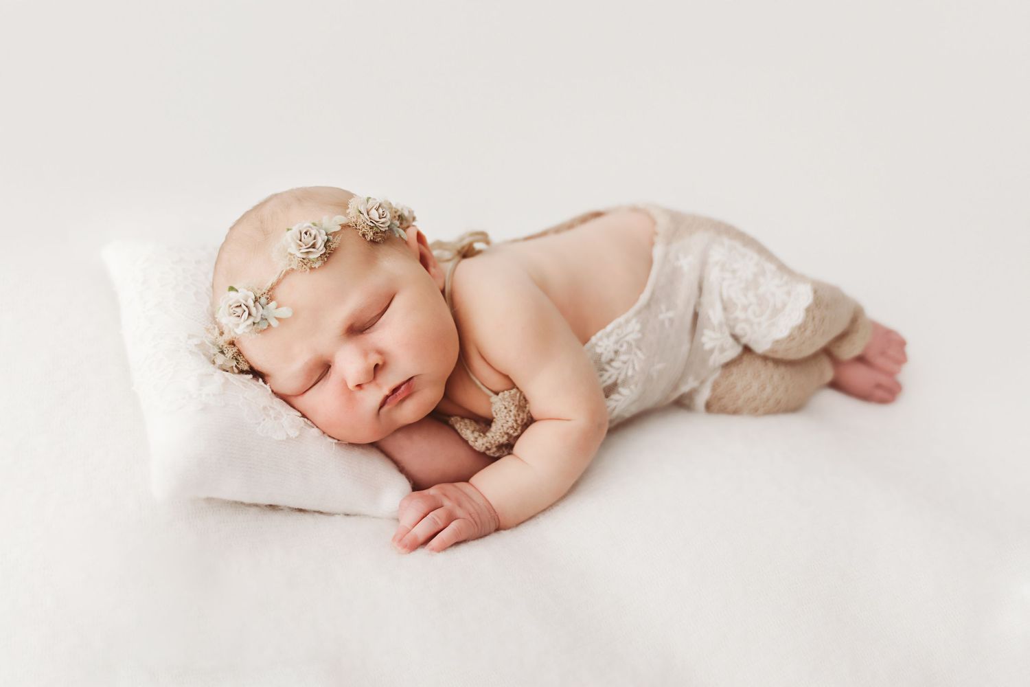 Peaceful newborn baby sleeping on a white pillow wearing lace bloomers and a jeweled headband.