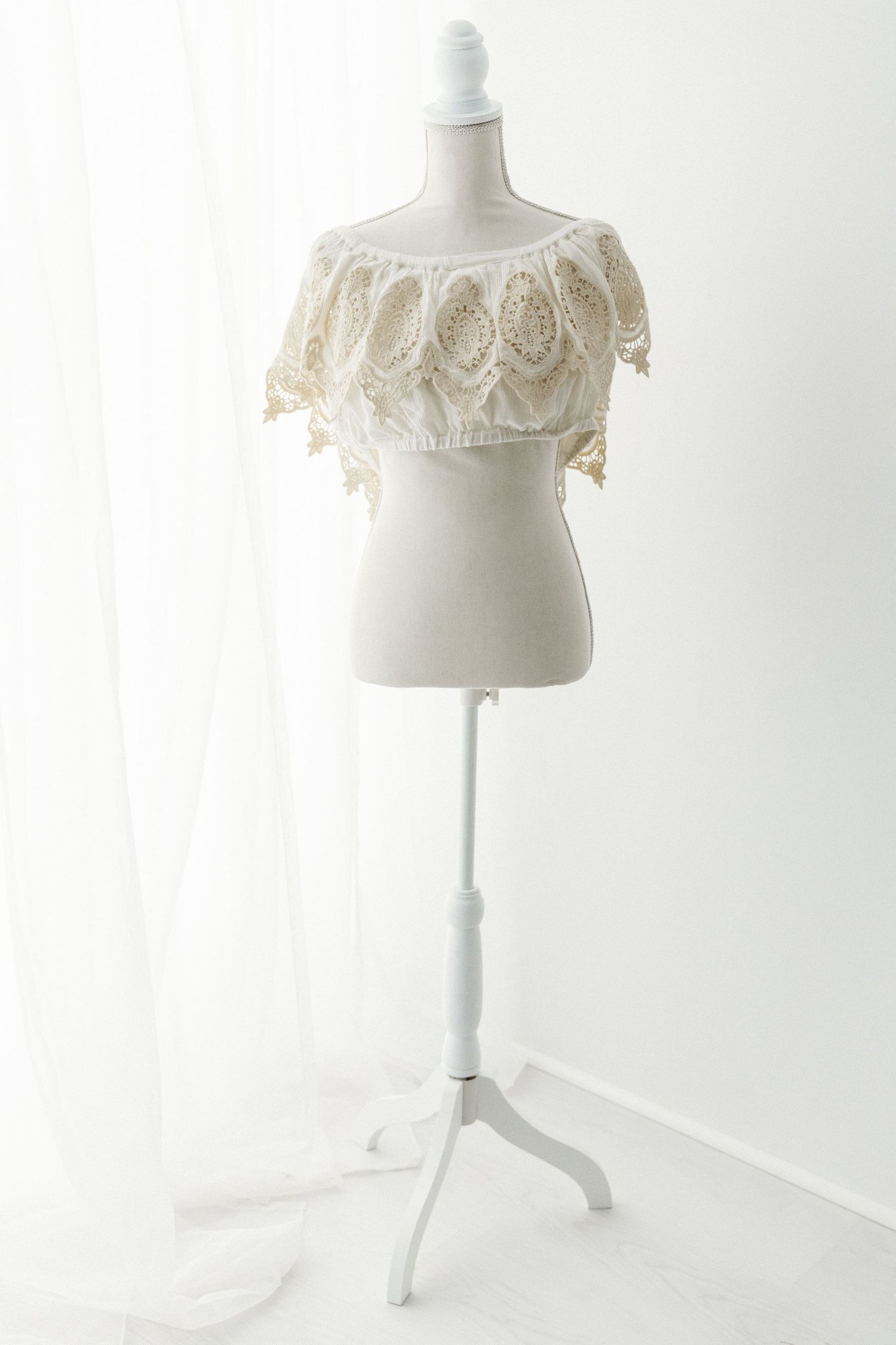White crochet lace off-shoulder crop top with scalloped hem on a mannequin stand.