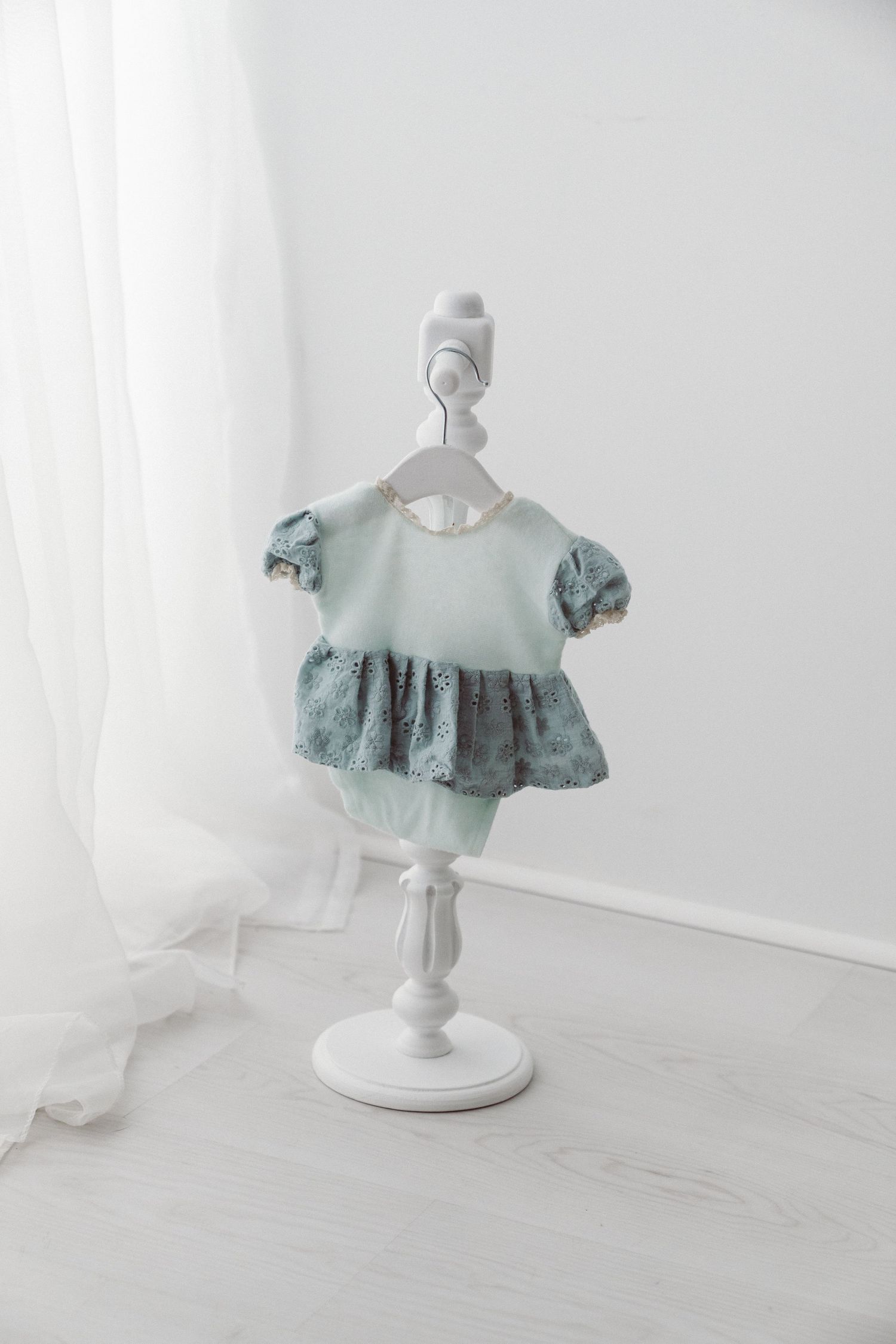 Mint green baby dress with lace detail and ruffled skirt displayed on a small white mannequin stand.