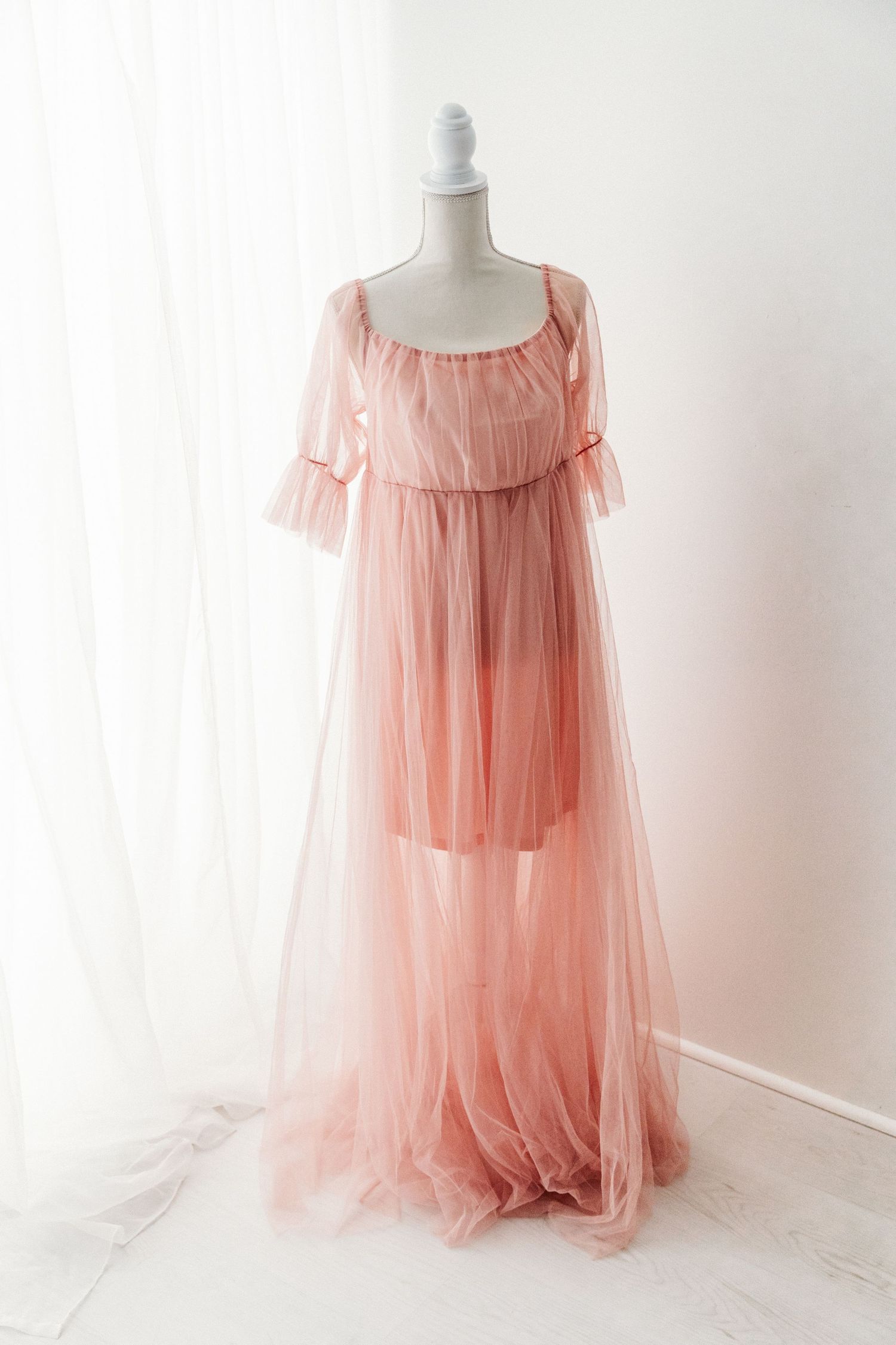 Sheer pink tulle off-shoulder maxi dress with ruffled overlay on a mannequin.