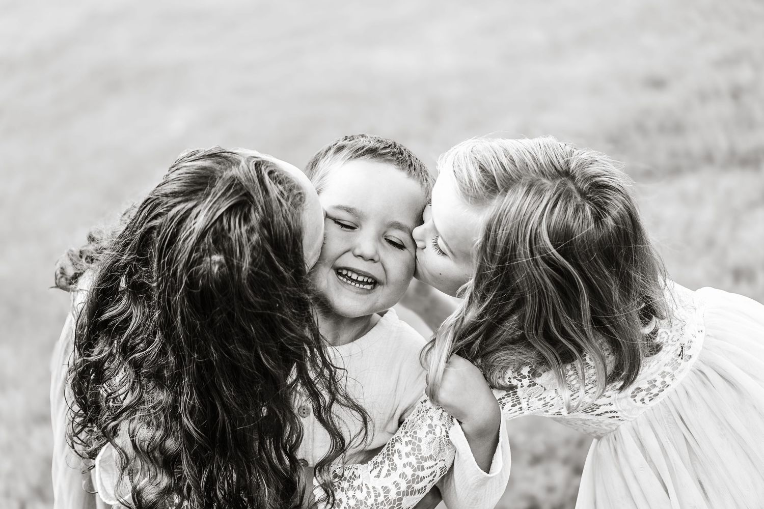 Black and white photo of two girls giving a laughing boy kisses on cheeks.