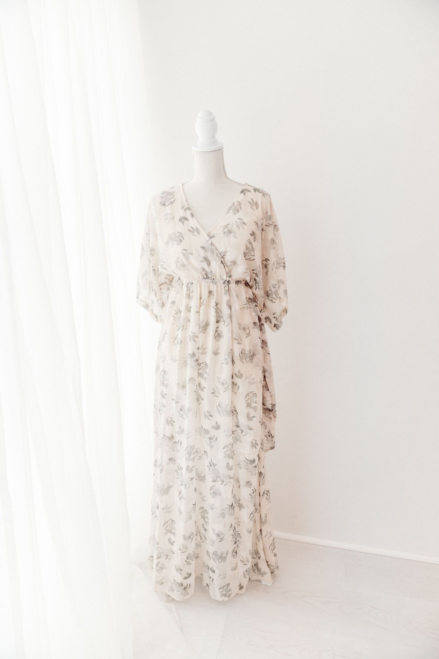 Ivory floral wrap maxi dress with flutter sleeves and tie waist displayed on a white mannequin.
