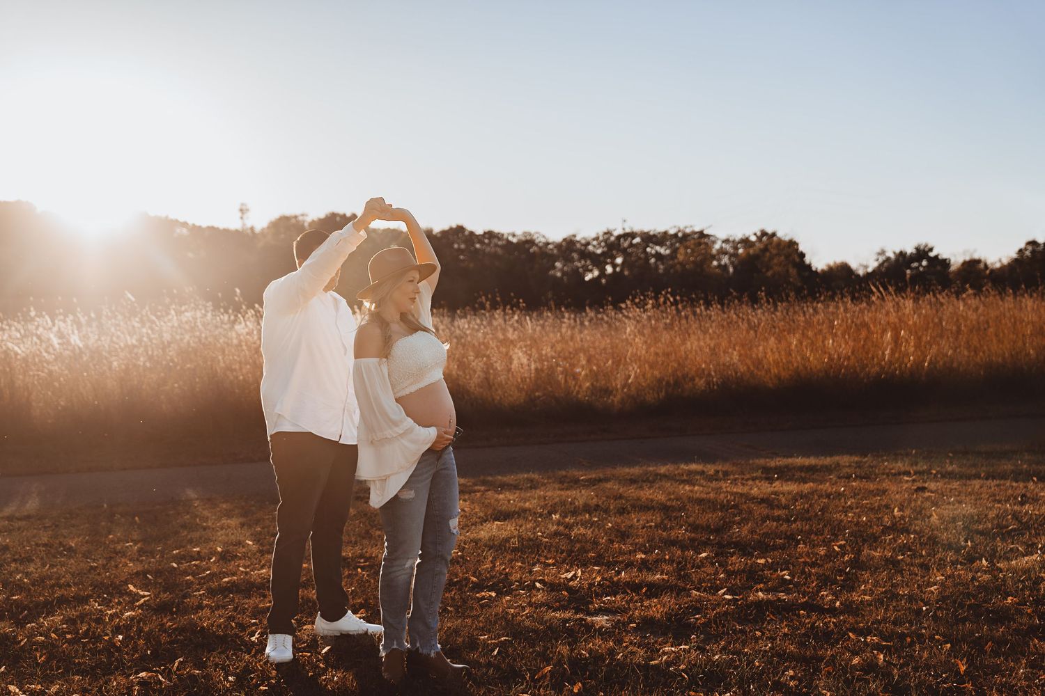 Couple embracing in a sunlit golden field during a maternity photoshoot at sunset.