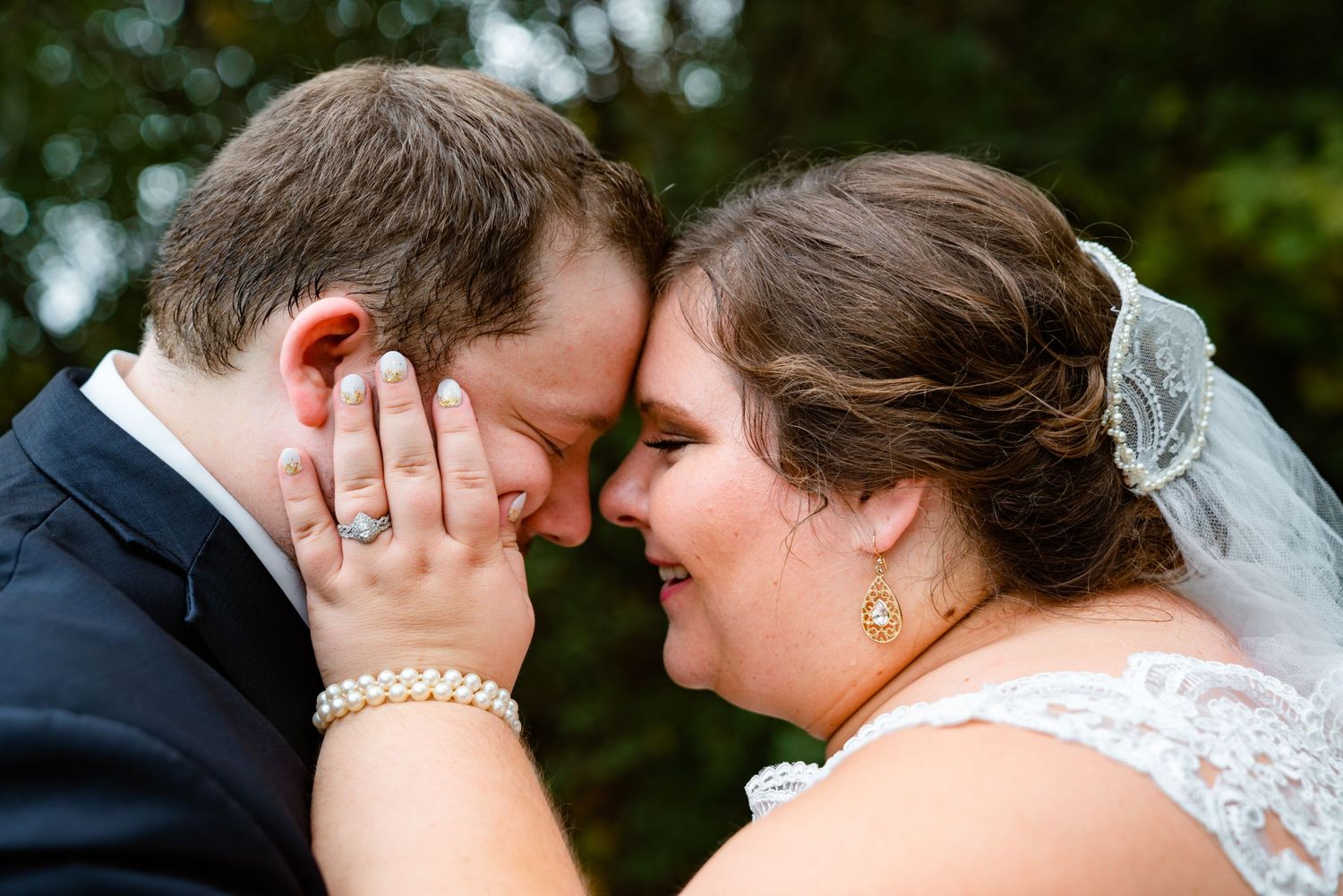 Bride and groom touching foreheads tenderly on their wedding day, bride wearing pearl bracelet and diamond ring.