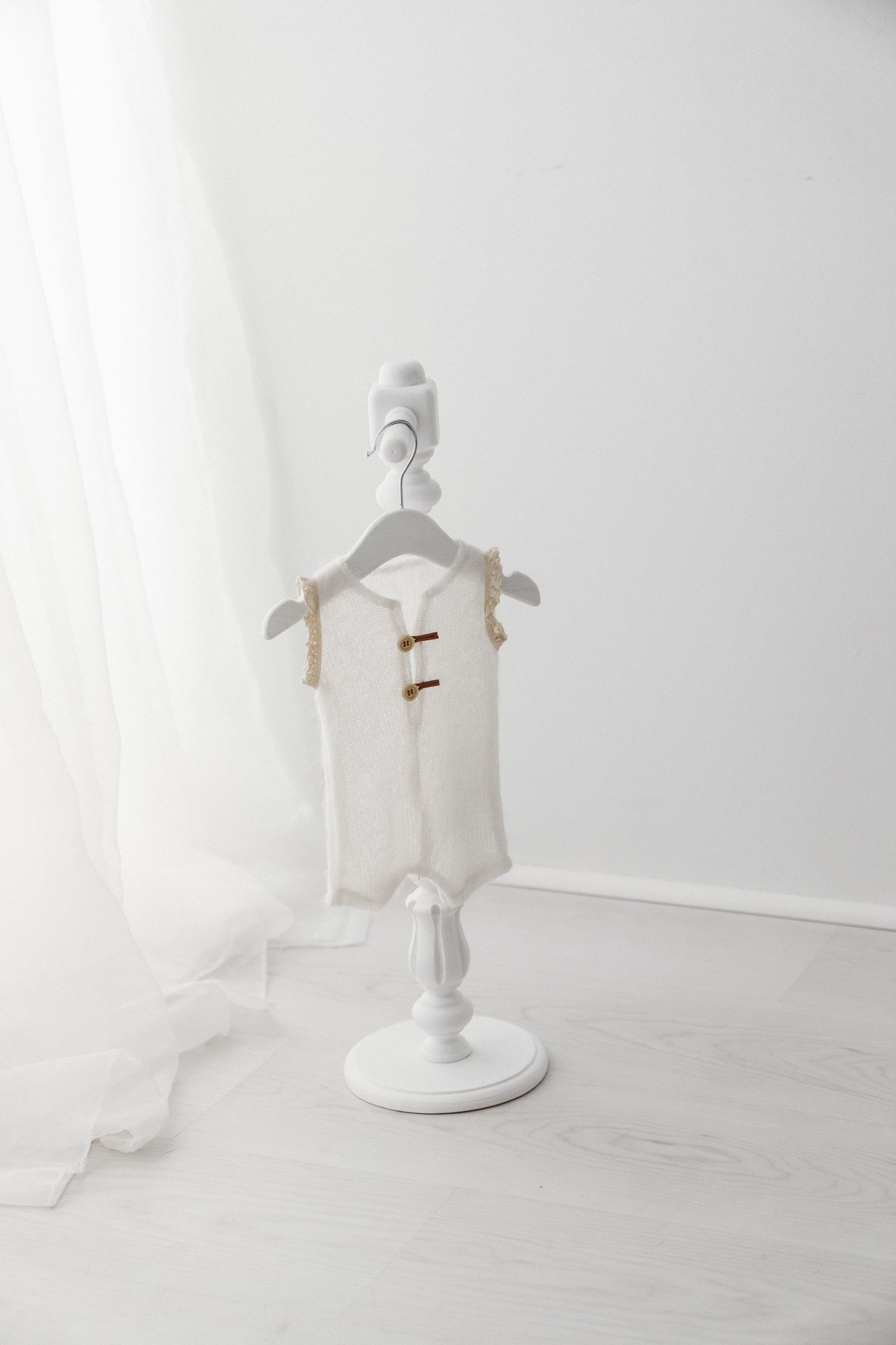 A white knit newborn vest with wooden buttons displayed on a small white dress form stand.