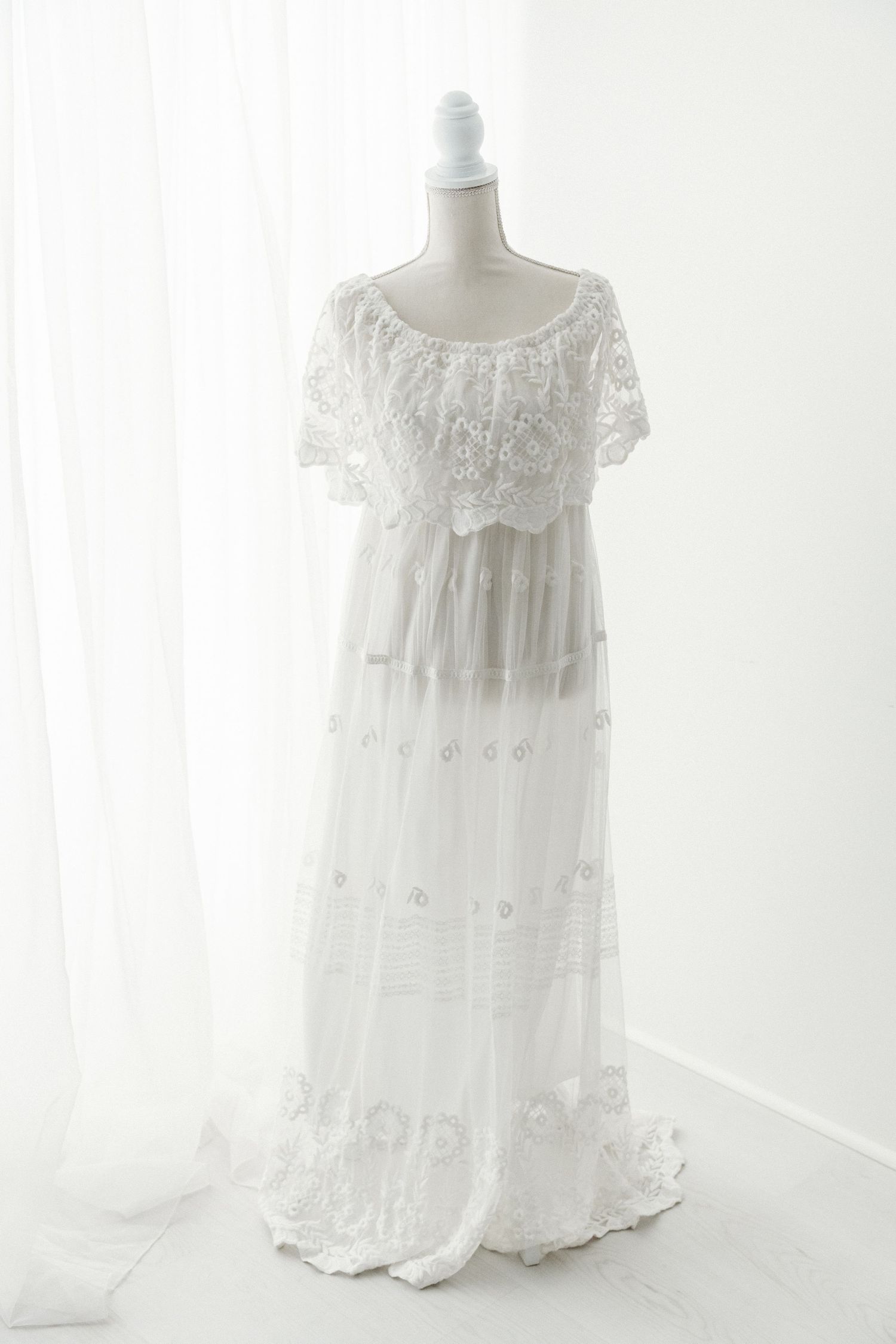 White lace and tulle off-shoulder maxi dress with floral embroidery on a mannequin.