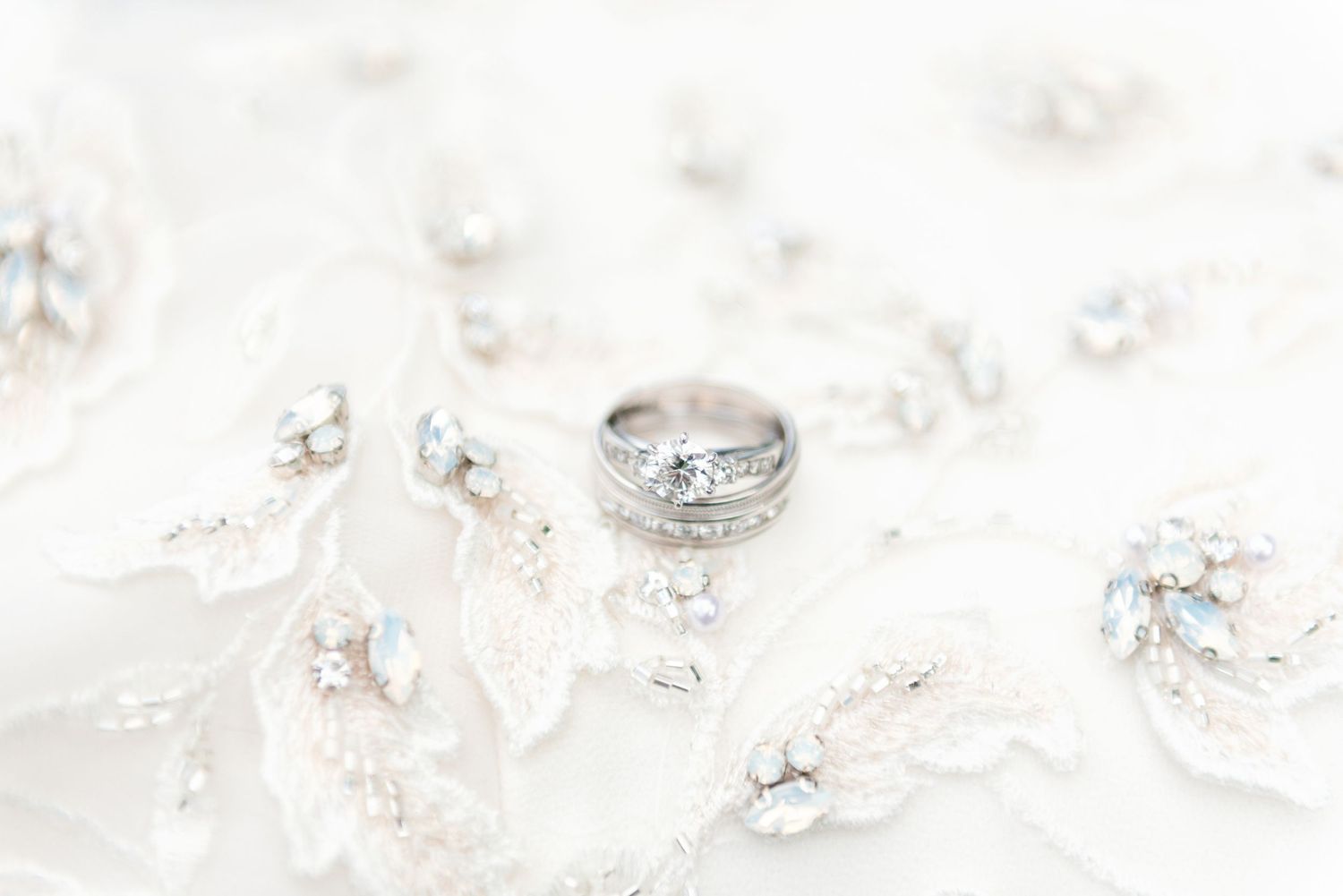 Diamond engagement ring displayed on white embroidered lace fabric with crystal embellishments.