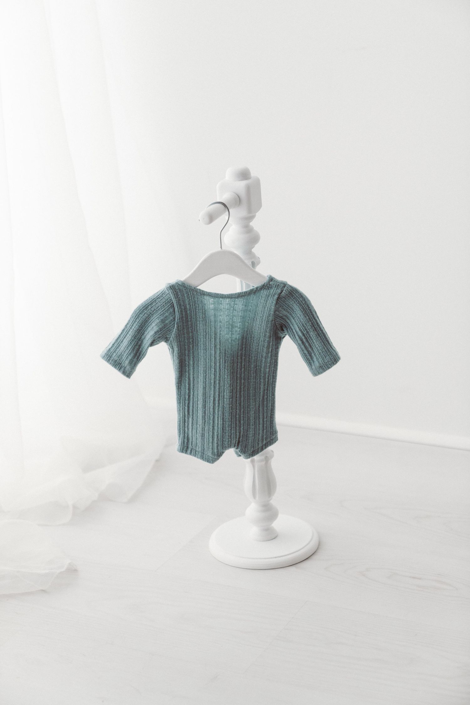 Teal ribbed short-sleeve baby bodysuit displayed on a white decorative hanger stand against a white background.