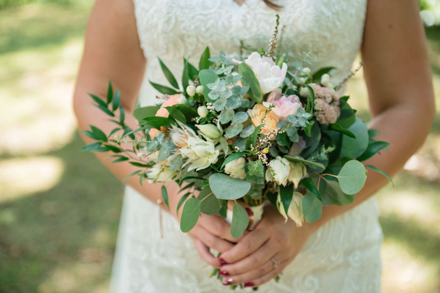 Bride holding a romantic bouquet of blush roses, white flowers, and eucalyptus greenery.