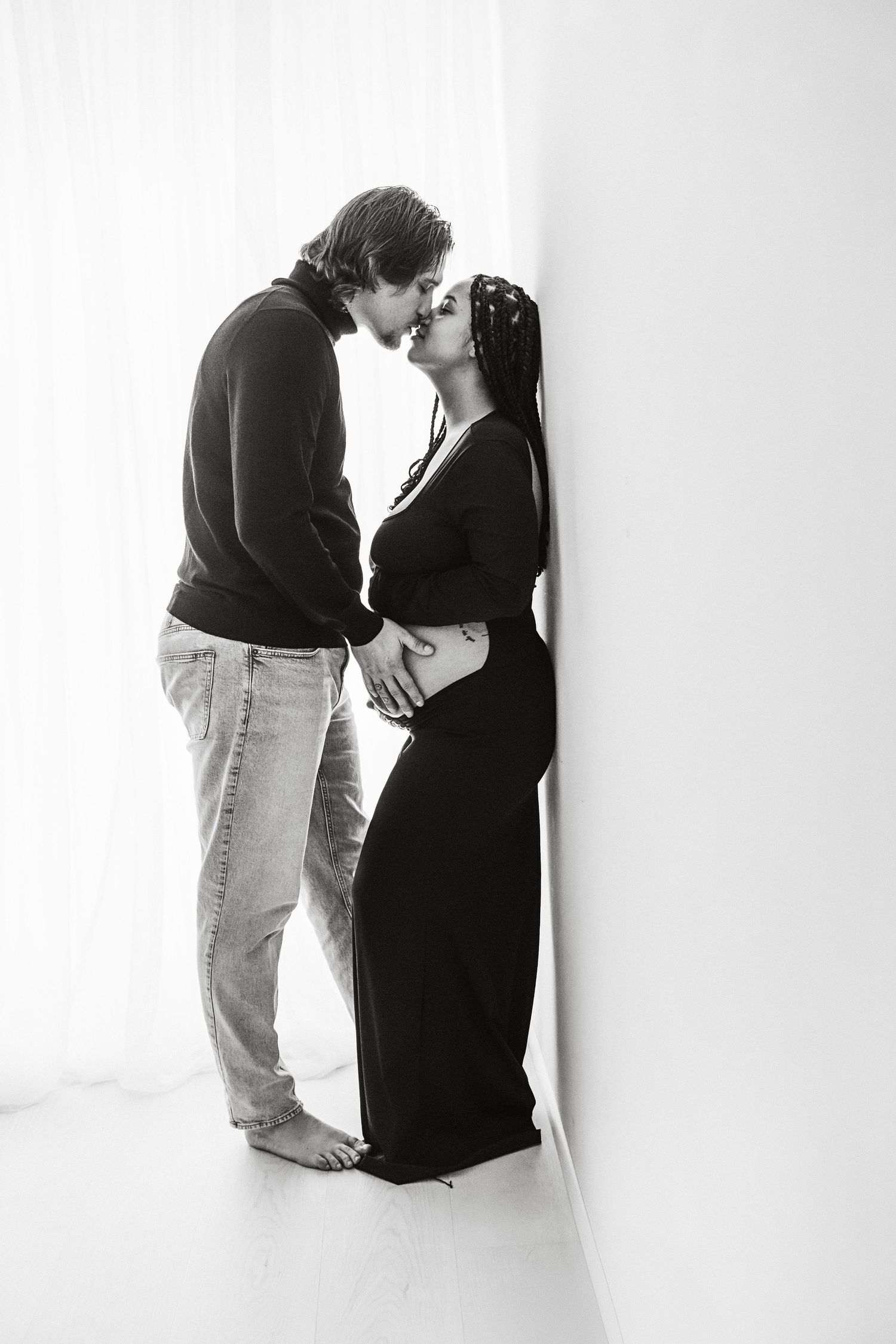 Black and white photo of a couple sharing a tender kiss, with the woman visibly pregnant in a black dress.