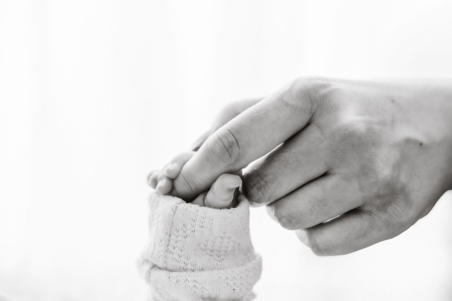 A black and white close-up of an adult hand gently holding a newborn baby's tiny feet.