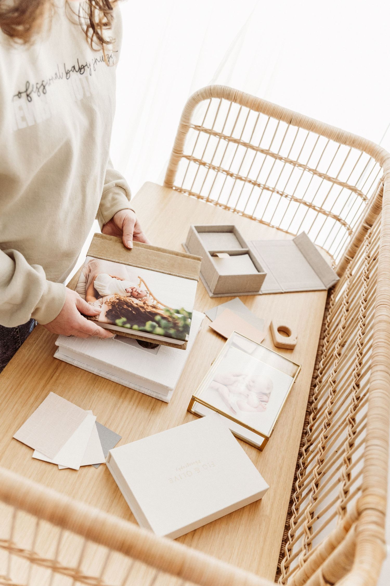 Woman arranging newborn photo albums and keepsake boxes on a wooden rattan table.