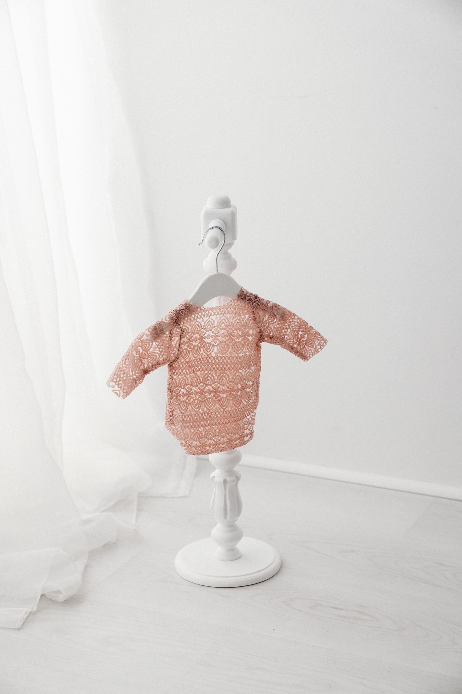 Pink patterned long-sleeve baby bodysuit with geometric design on a white decorative mini stand.