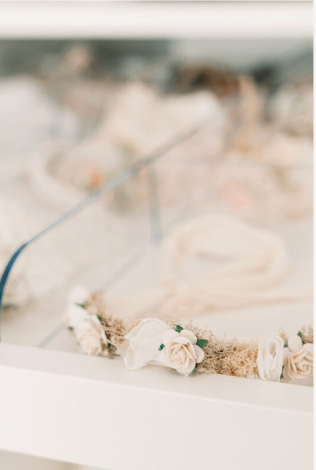 Delicate floral crown with white roses and dried moss displayed in a glass case for a wedding.