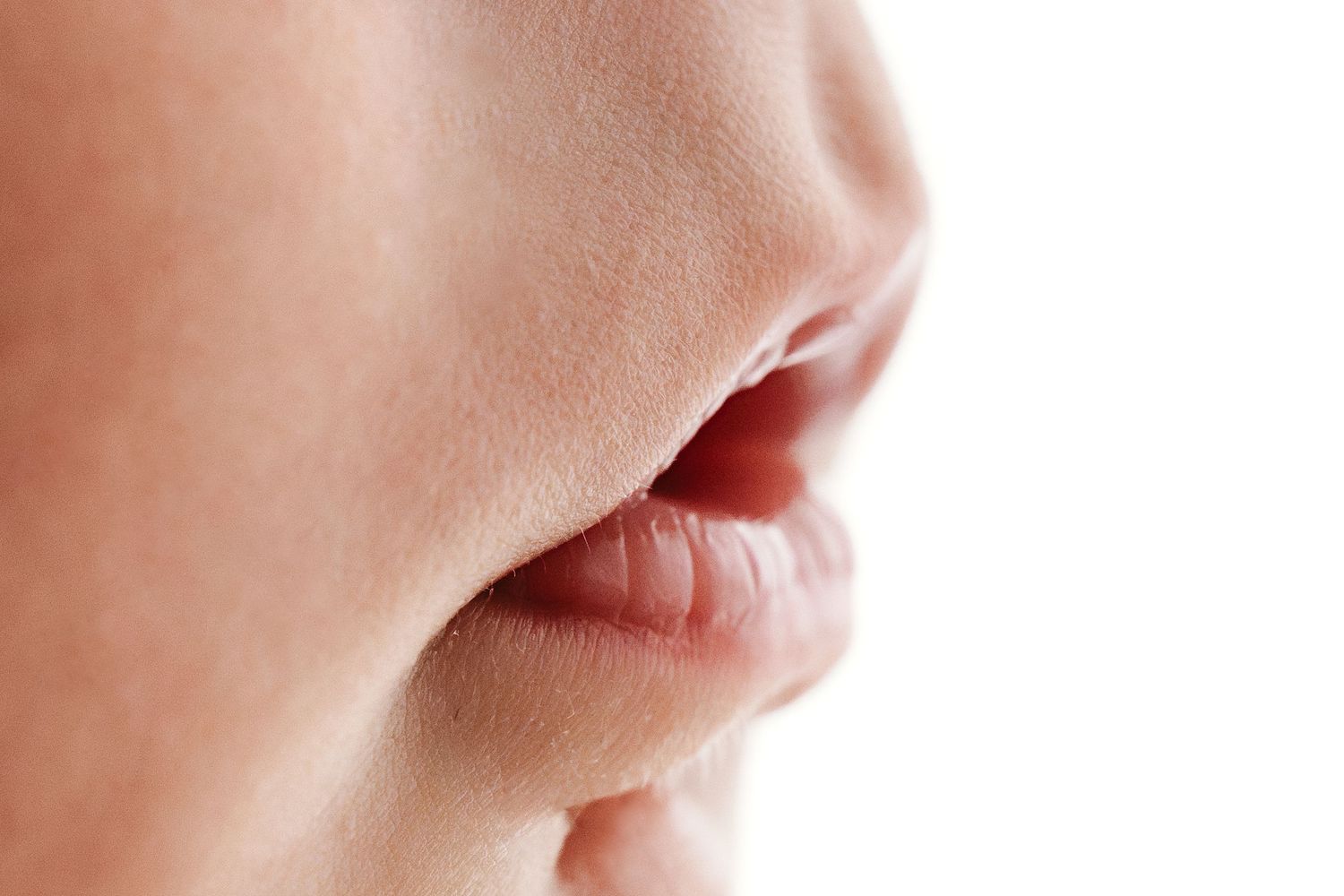 Extreme close-up of a newborn baby's nose and slightly open lips on white background.