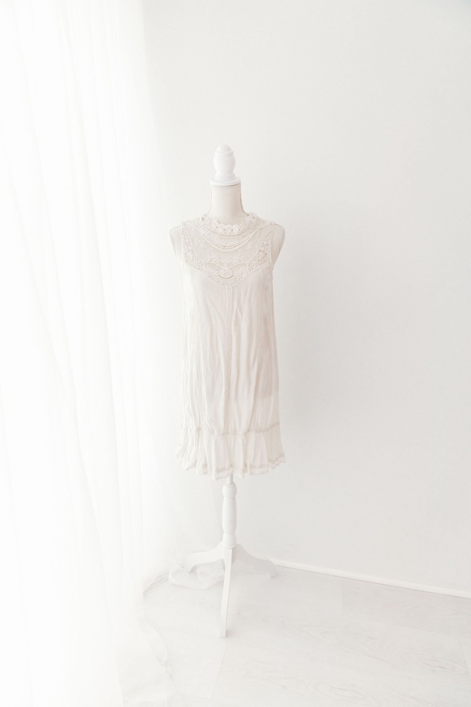 White sleeveless mini dress with lace yoke and ruffled hem on white mannequin.
