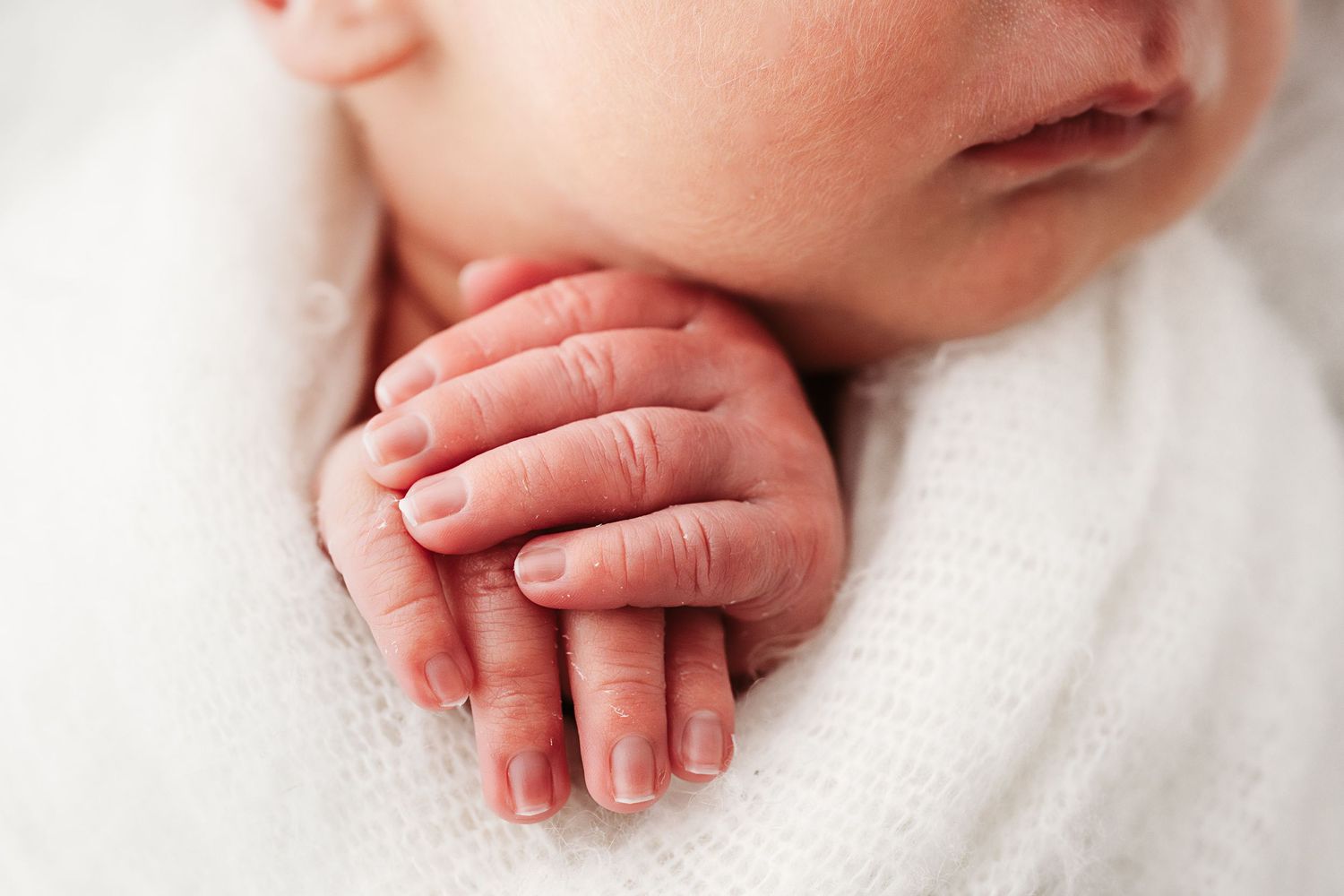 Close-up of a newborn baby's tiny delicate hands resting on a soft white blanket.