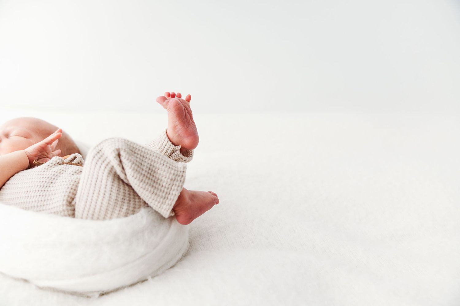 Newborn baby in striped romper with tiny feet raised up on white background.