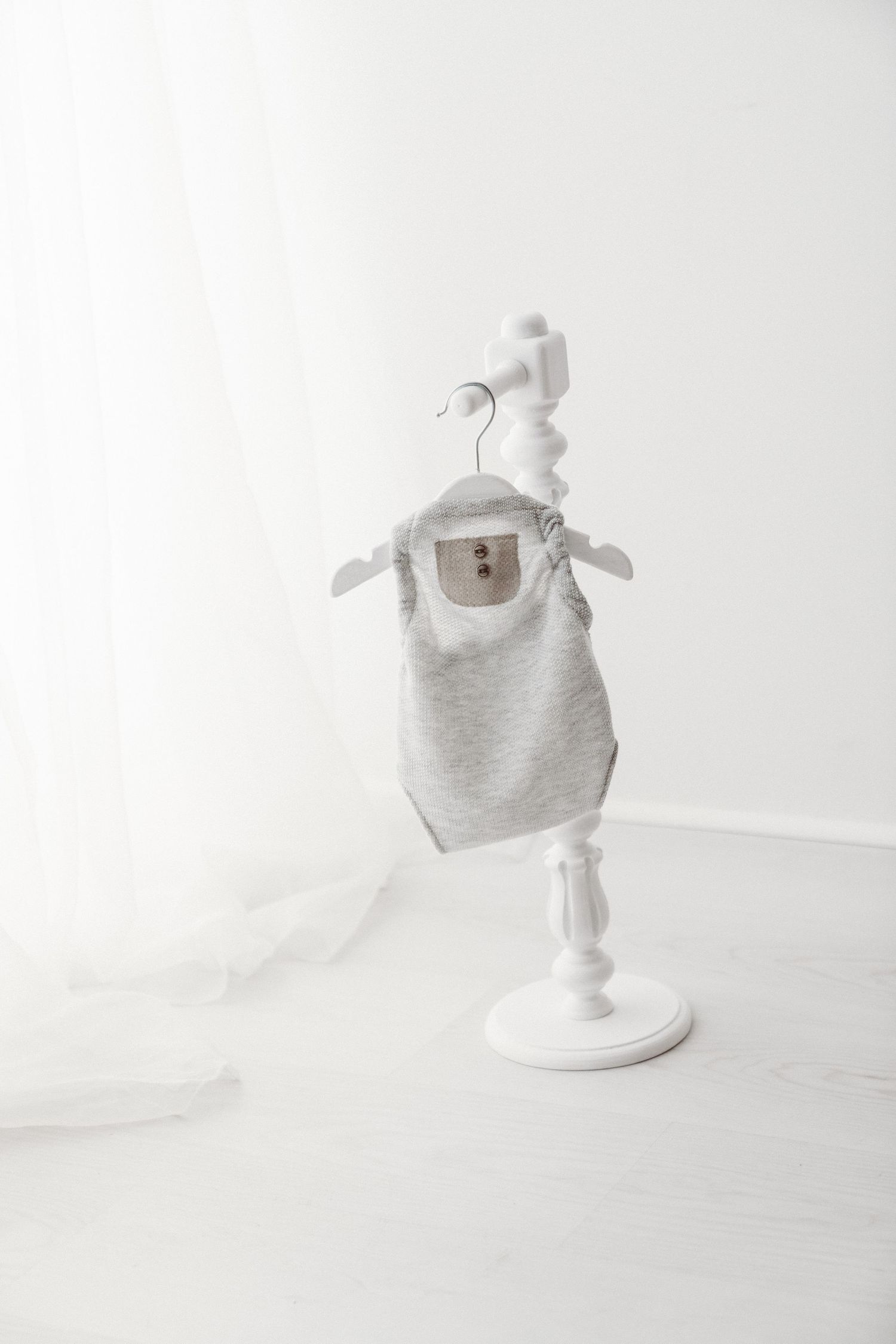 Gray sleeveless baby bodysuit with button detail displayed on a white decorative hanger stand.
