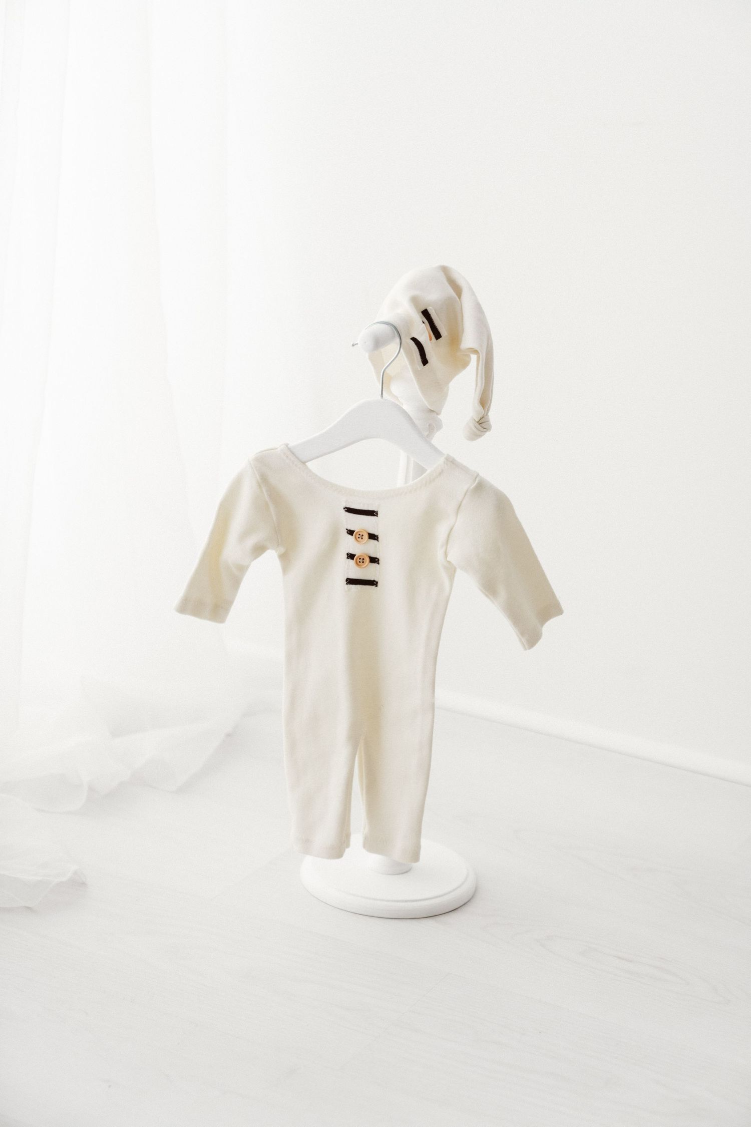 Ivory knit baby sleepsuit with striped chest detail and pointed bonnet displayed on white hanger stand.