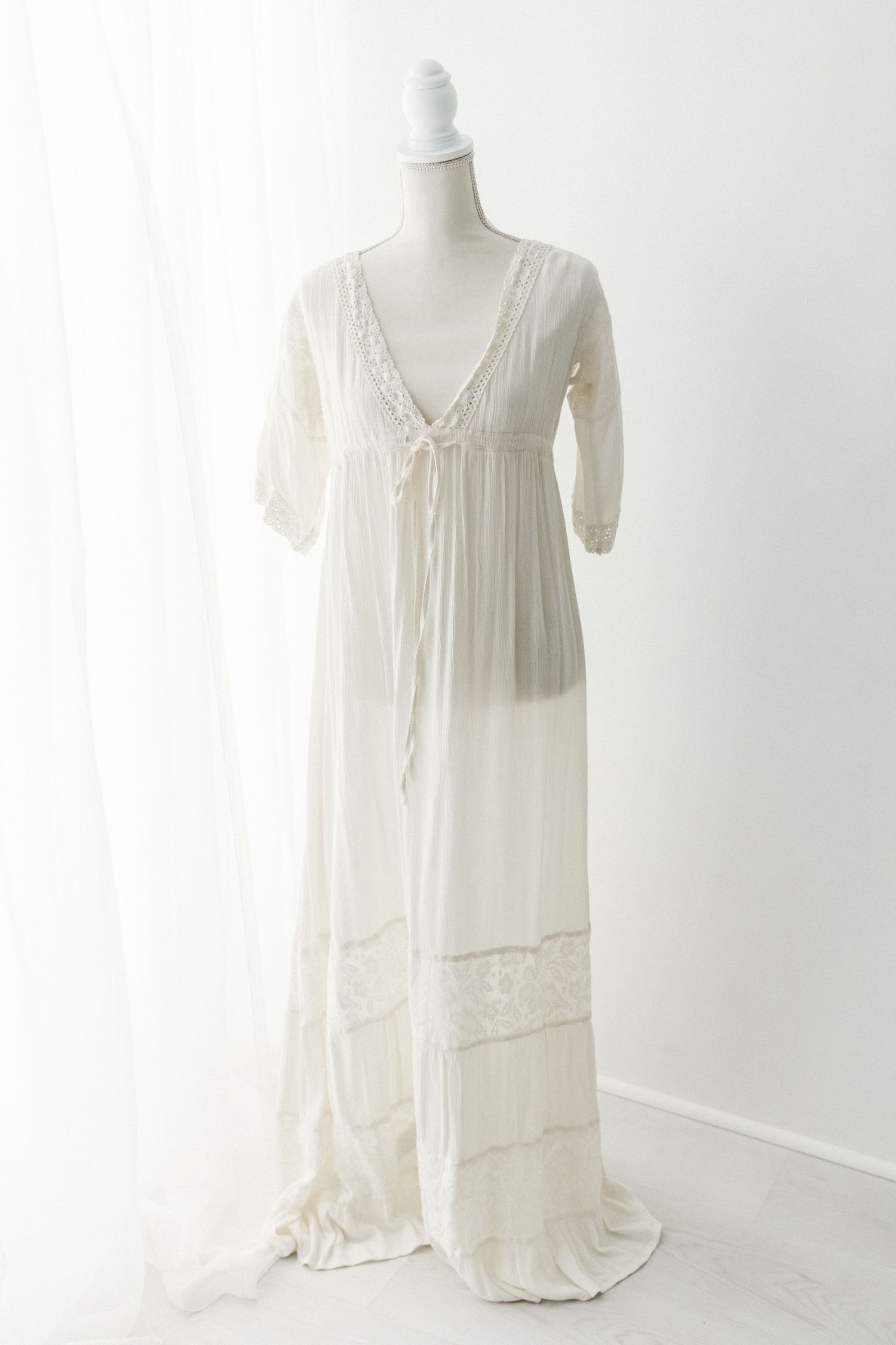 Ivory bohemian maxi dress with V-neck, lace trim, and three-quarter sleeves on mannequin.