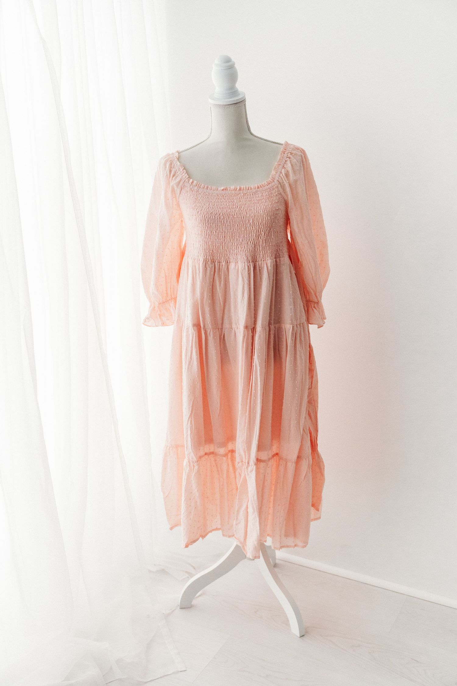 Peach smocked bodice midi dress with puff sleeves and tiered skirt on mannequin.