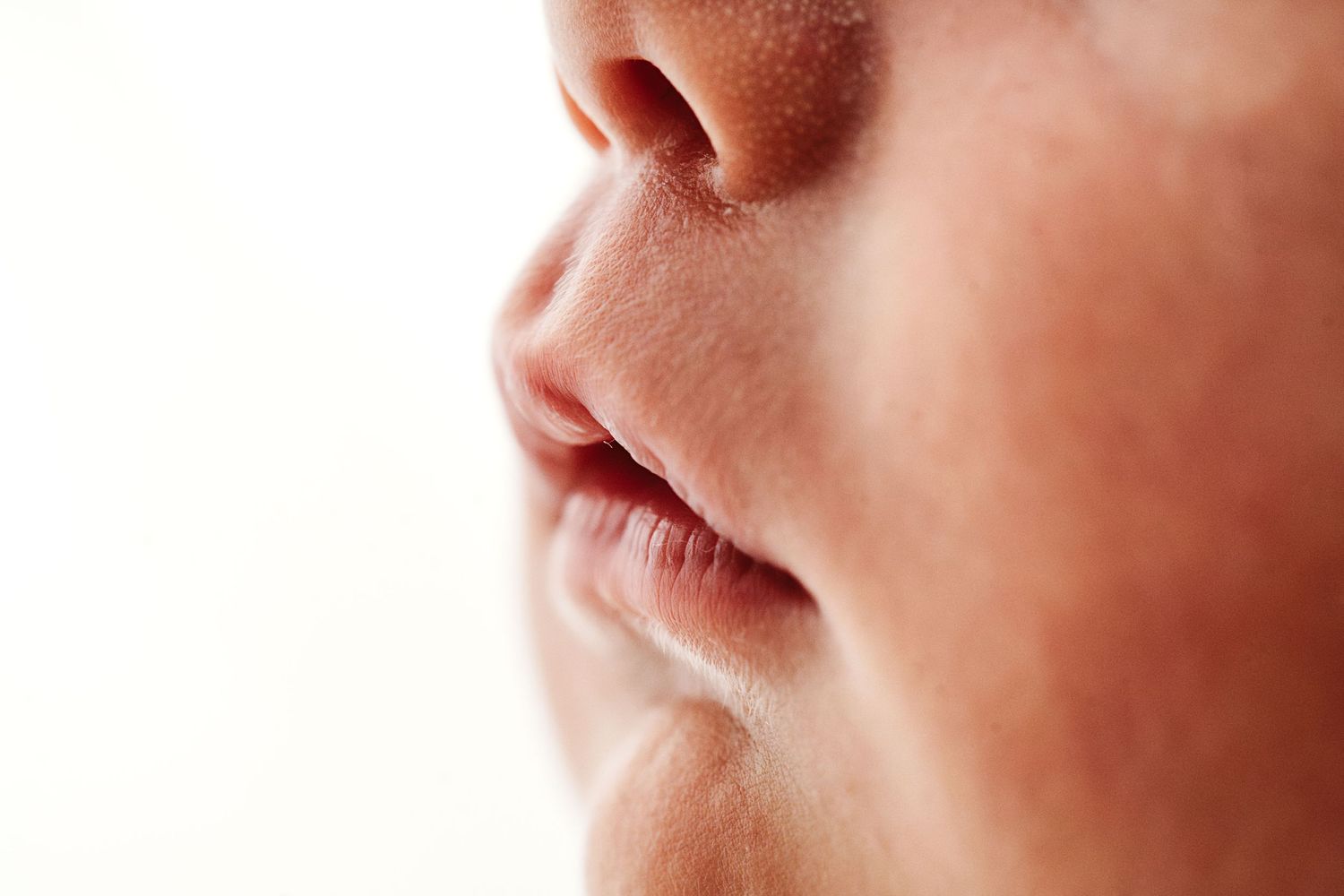 Extreme close-up profile view of a newborn baby's nose and lips on white background.