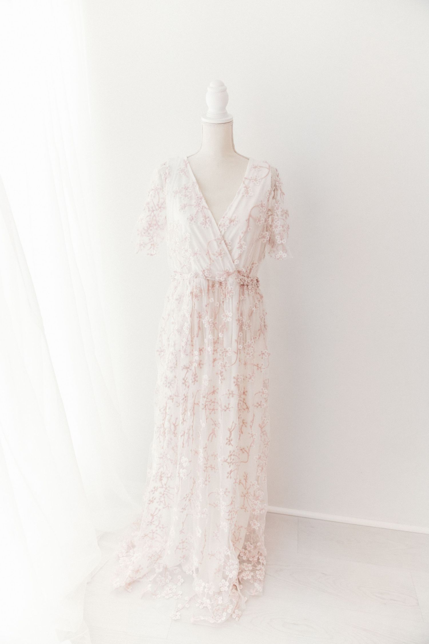 Elegant blush floral lace maxi gown with V-neckline on white mannequin.