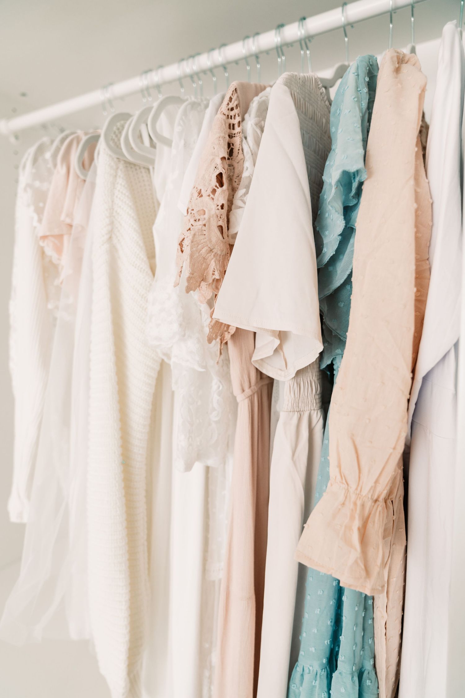 Collection of soft pastel maternity dresses in white, pink, and blue on a clothing rack.