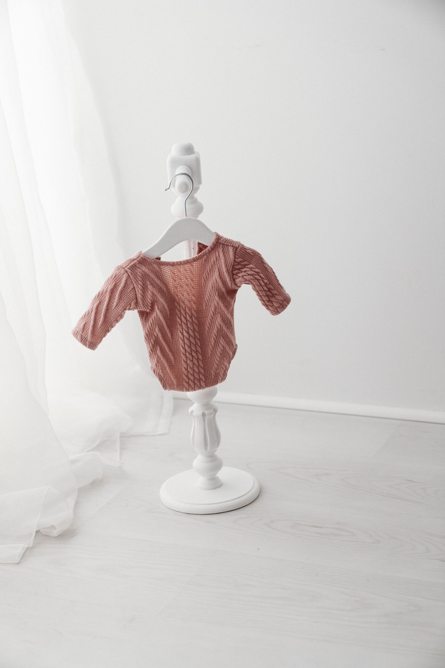 Pink cable-knit baby sweater with short sleeves displayed on a white decorative mini clothes stand in a white room.