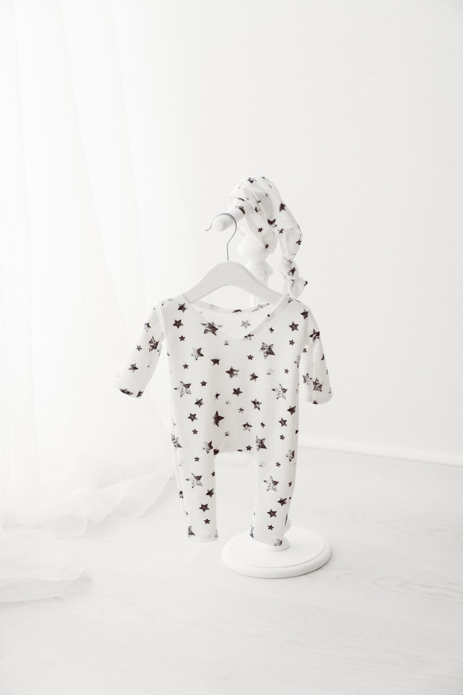 White star-print baby footed sleeper with matching knotted hat displayed on a white decorative stand.