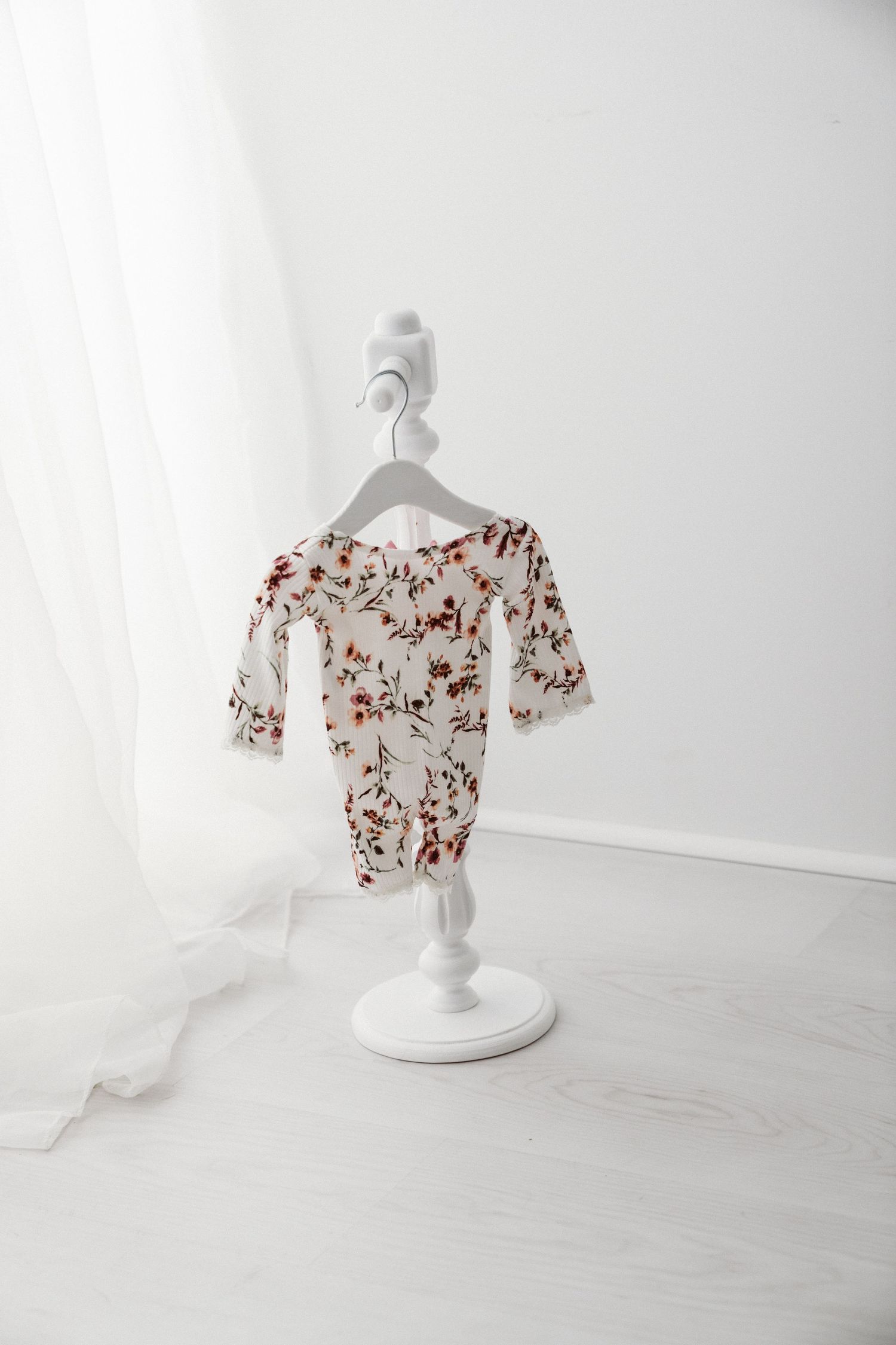 Floral print baby bodysuit with long sleeves displayed on a white decorative mini clothes stand in a bright white room.