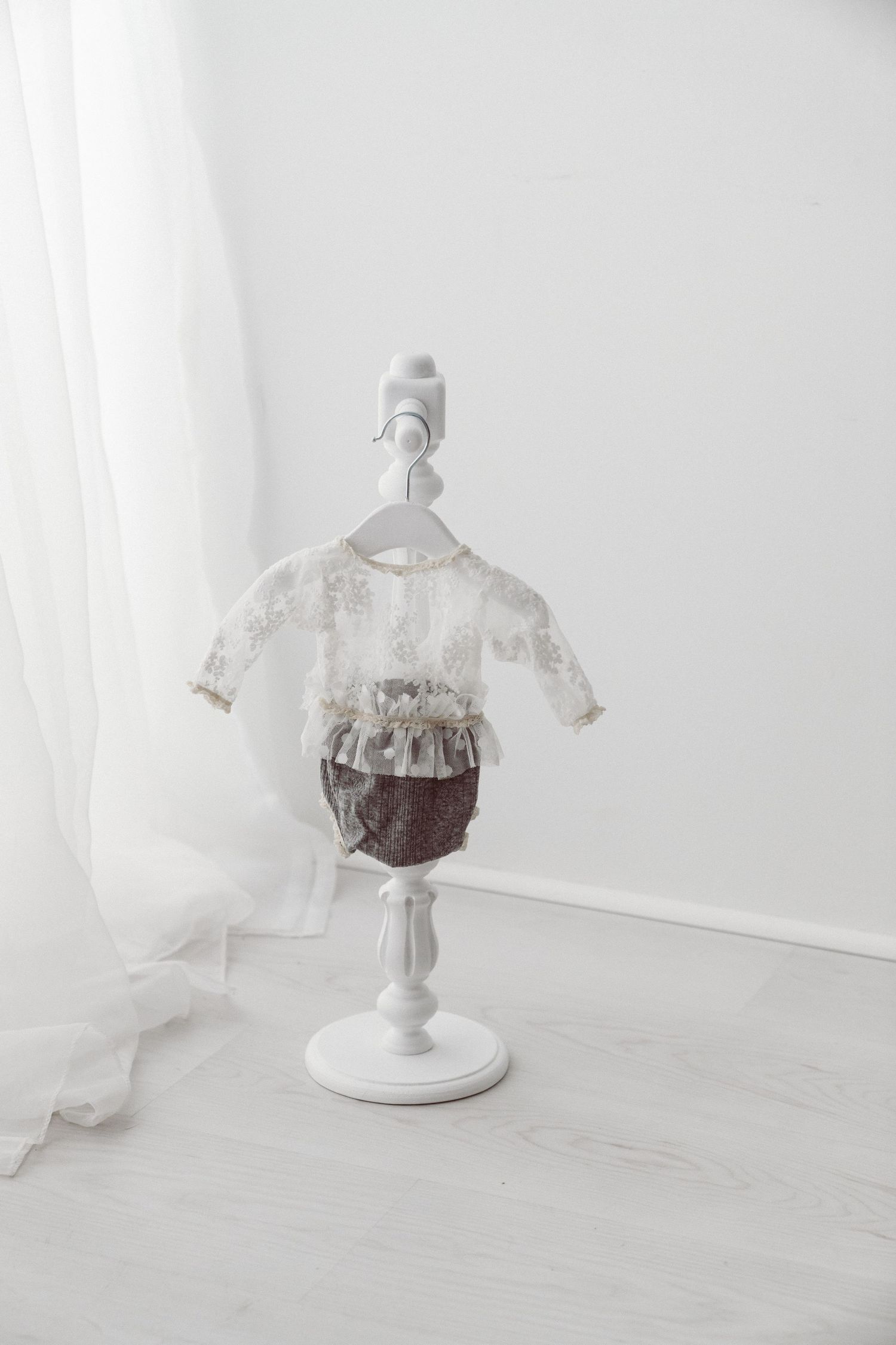 White lace top and brown knit bloomer baby outfit on a decorative white mini stand in a bright white studio room.