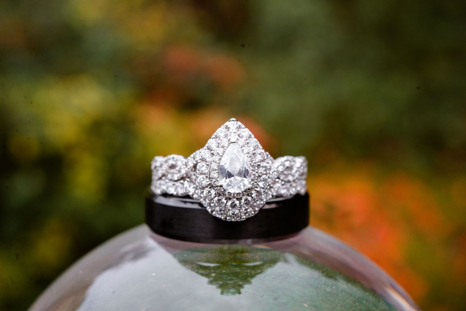 Elegant pear-shaped diamond halo engagement ring with wedding bands displayed on a reflective surface.