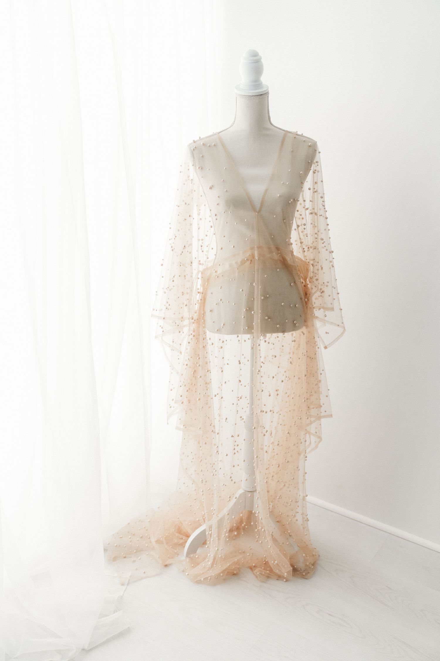 Champagne sheer tulle robe with gold sequin embellishments and flowing train on mannequin.