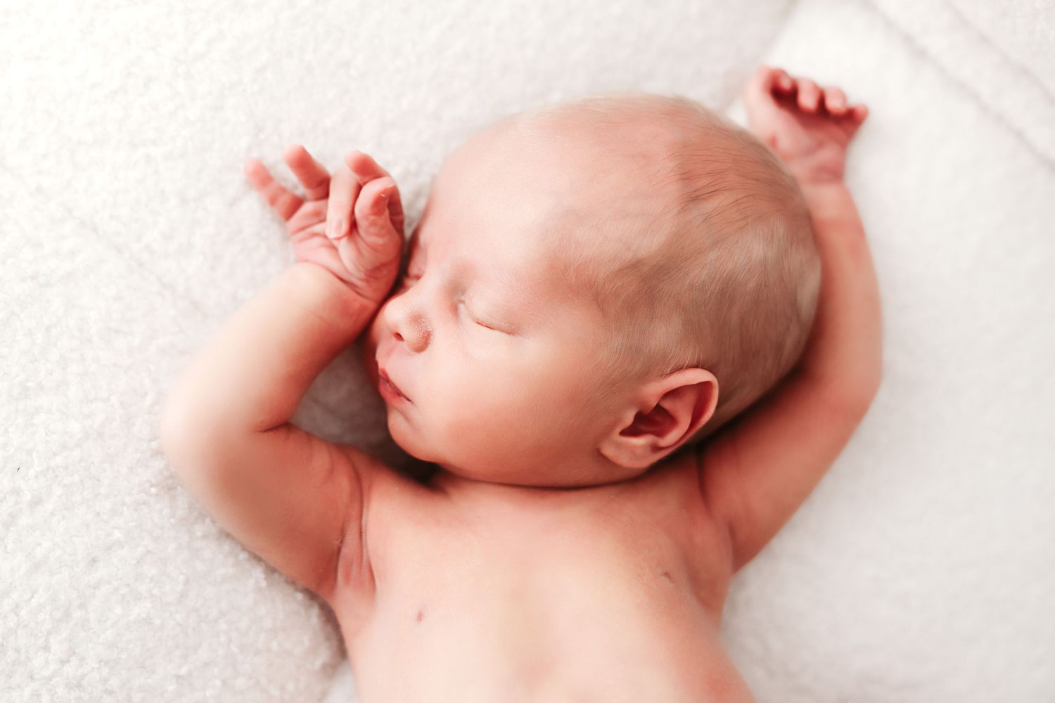 Peaceful newborn baby sleeping on a soft white blanket with arms stretched out.