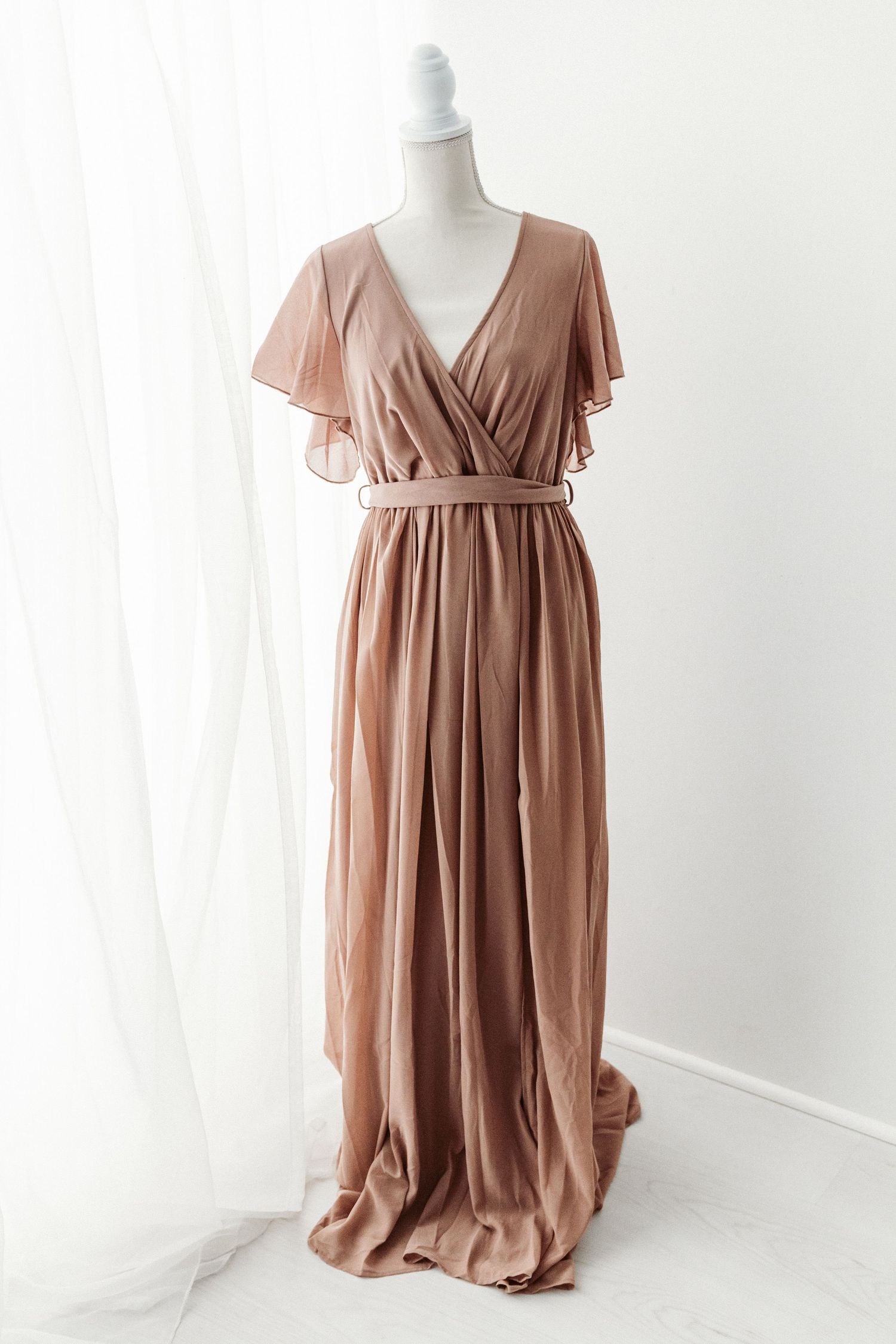 Dusty rose chiffon wrap maxi dress with flutter sleeves and belted waist on mannequin.