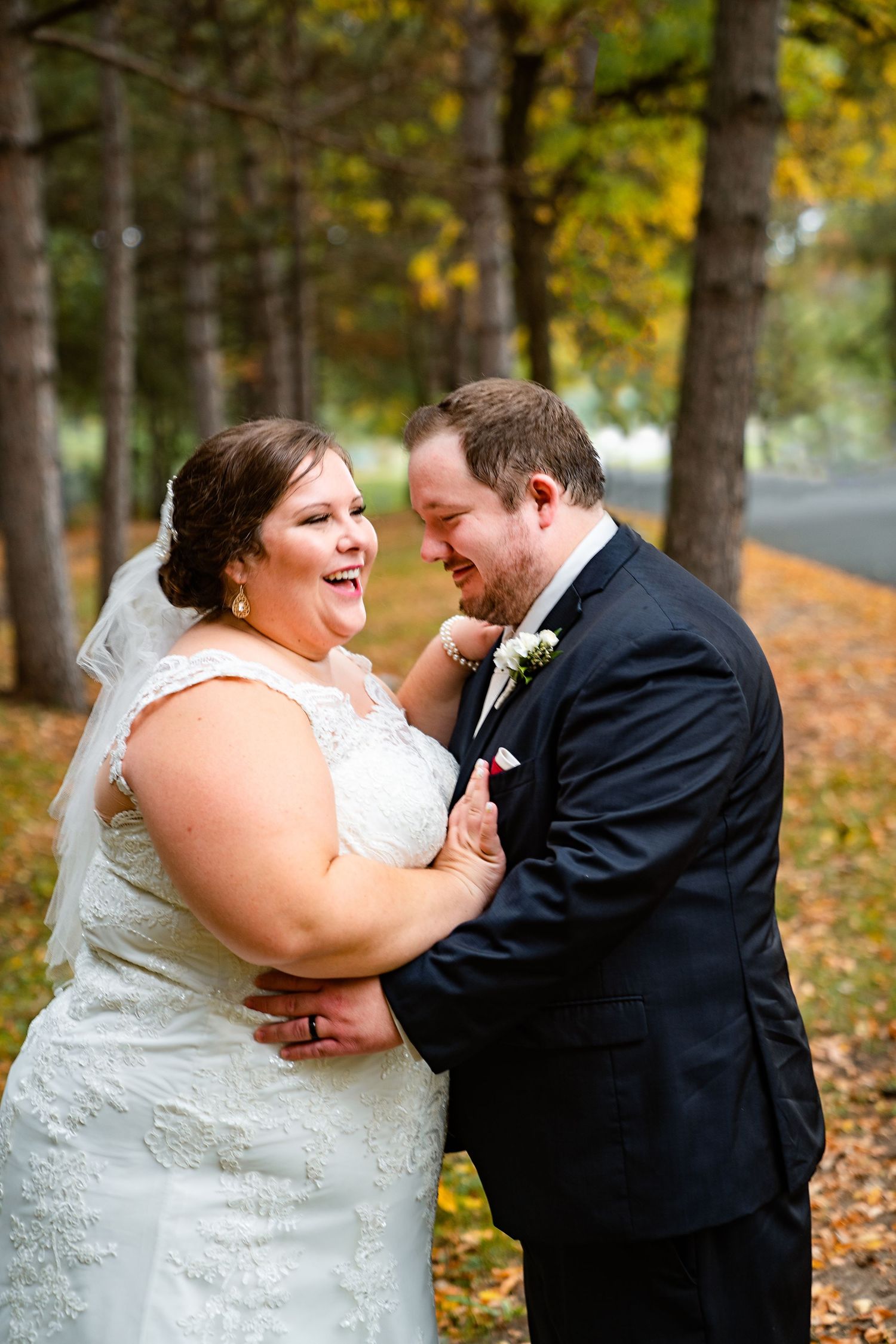 Laughing bride and groom sharing a joyful moment together among autumn trees in fall wedding photos.