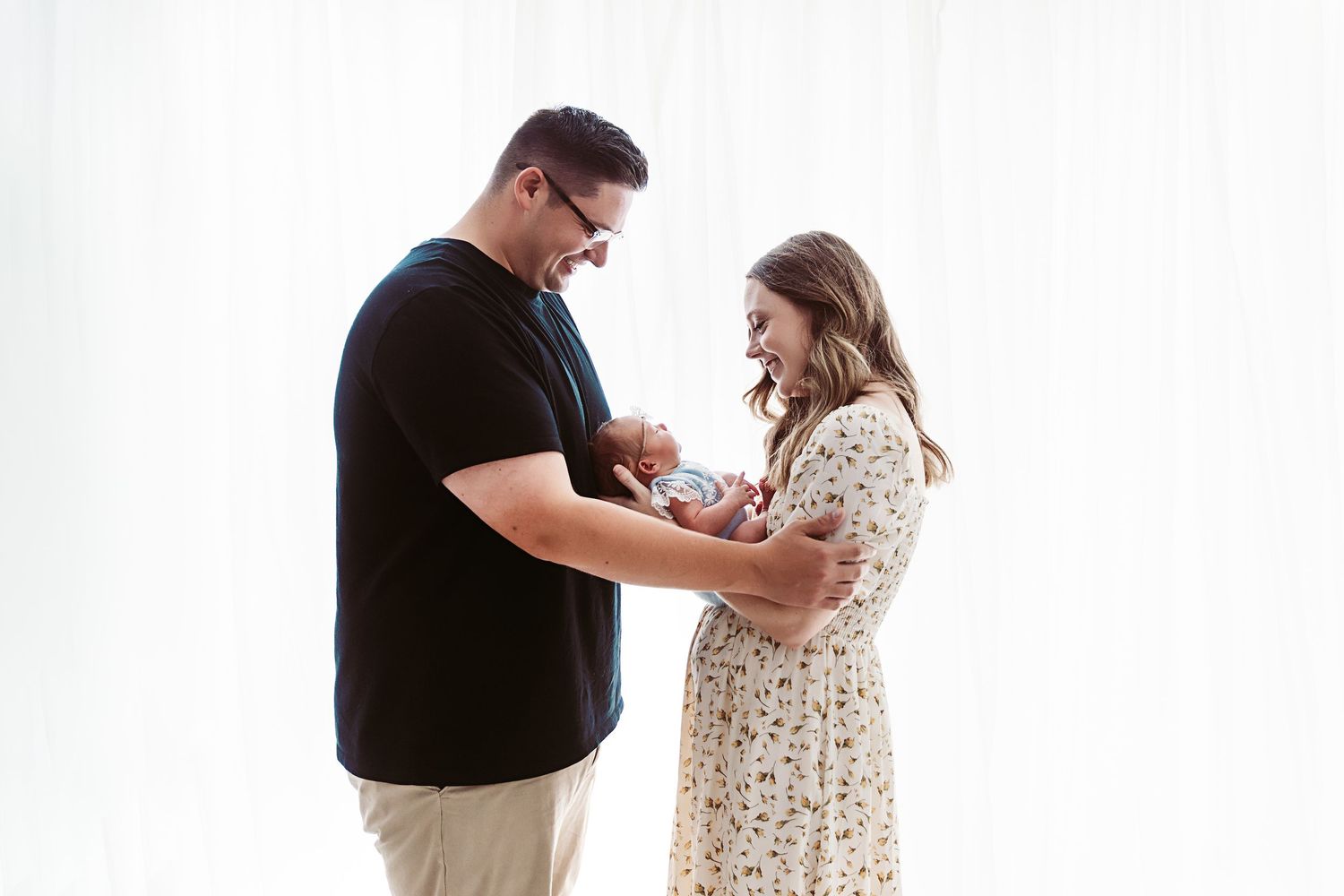 New parents standing together sharing a tender moment while holding their newborn baby.