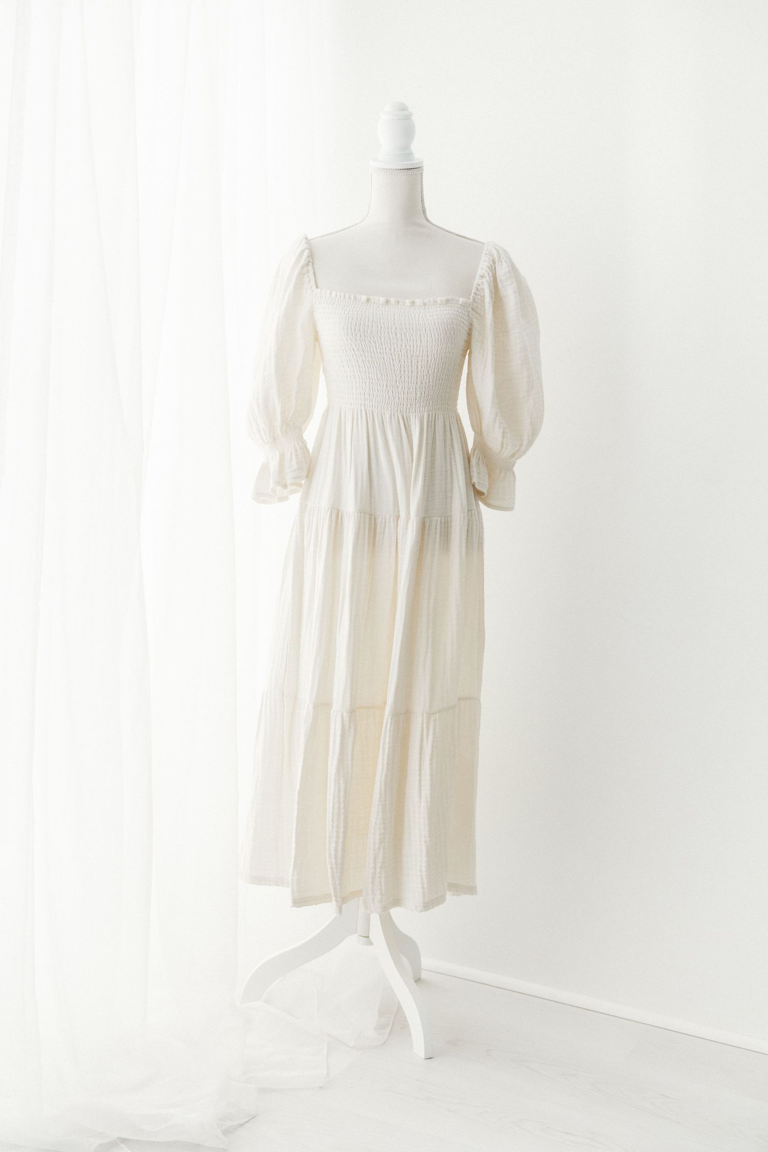 Cream smocked bodice puff sleeve midi dress with tiered skirt on mannequin.